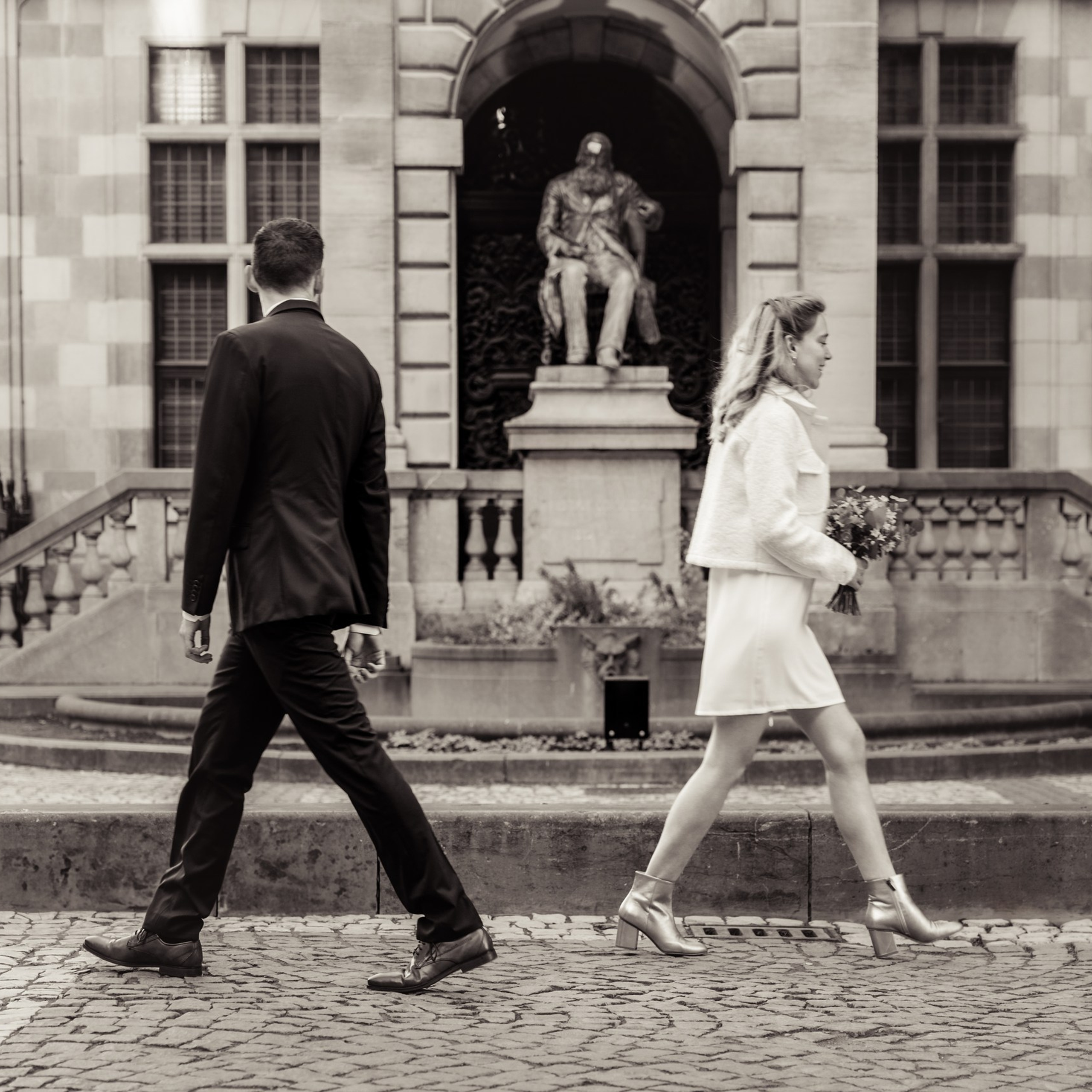Bruidspaar loopt langs elkaar voor een historisch gebouw in zwart-wit