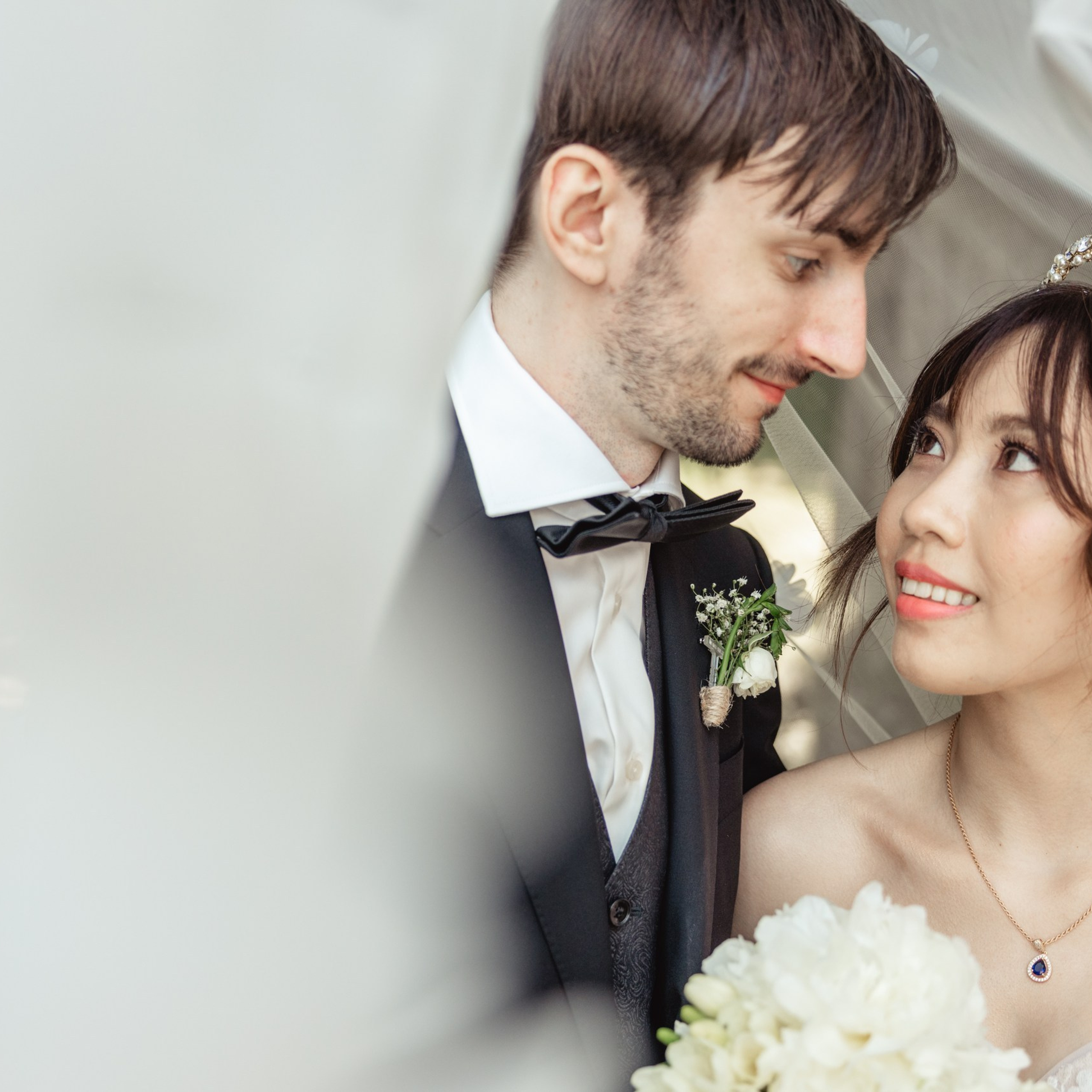 Bruidspaar kijkt elkaar glimlachend aan onder een sluier