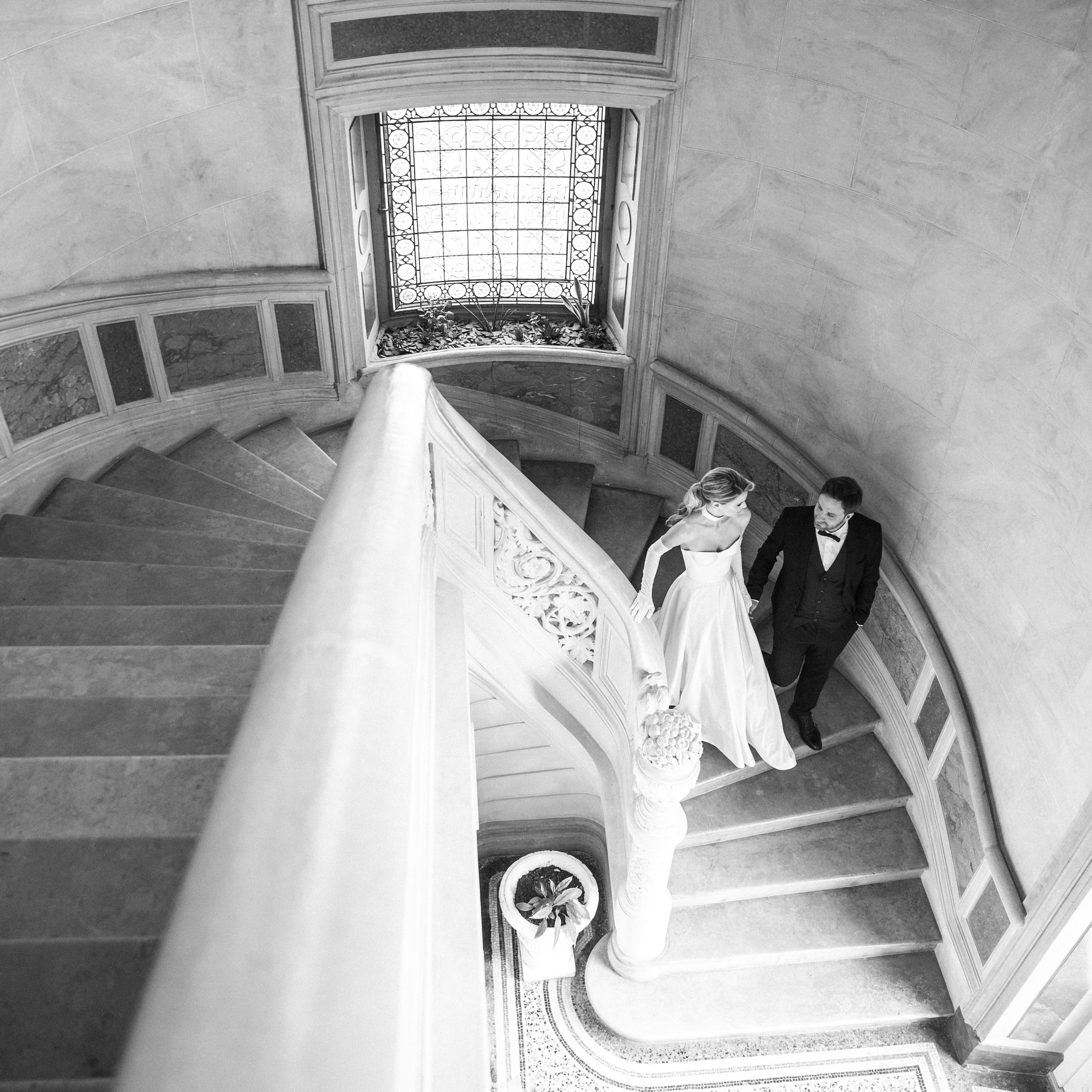 The groom is helping the bride walk down the staircase in a historical wedding venue in Spain