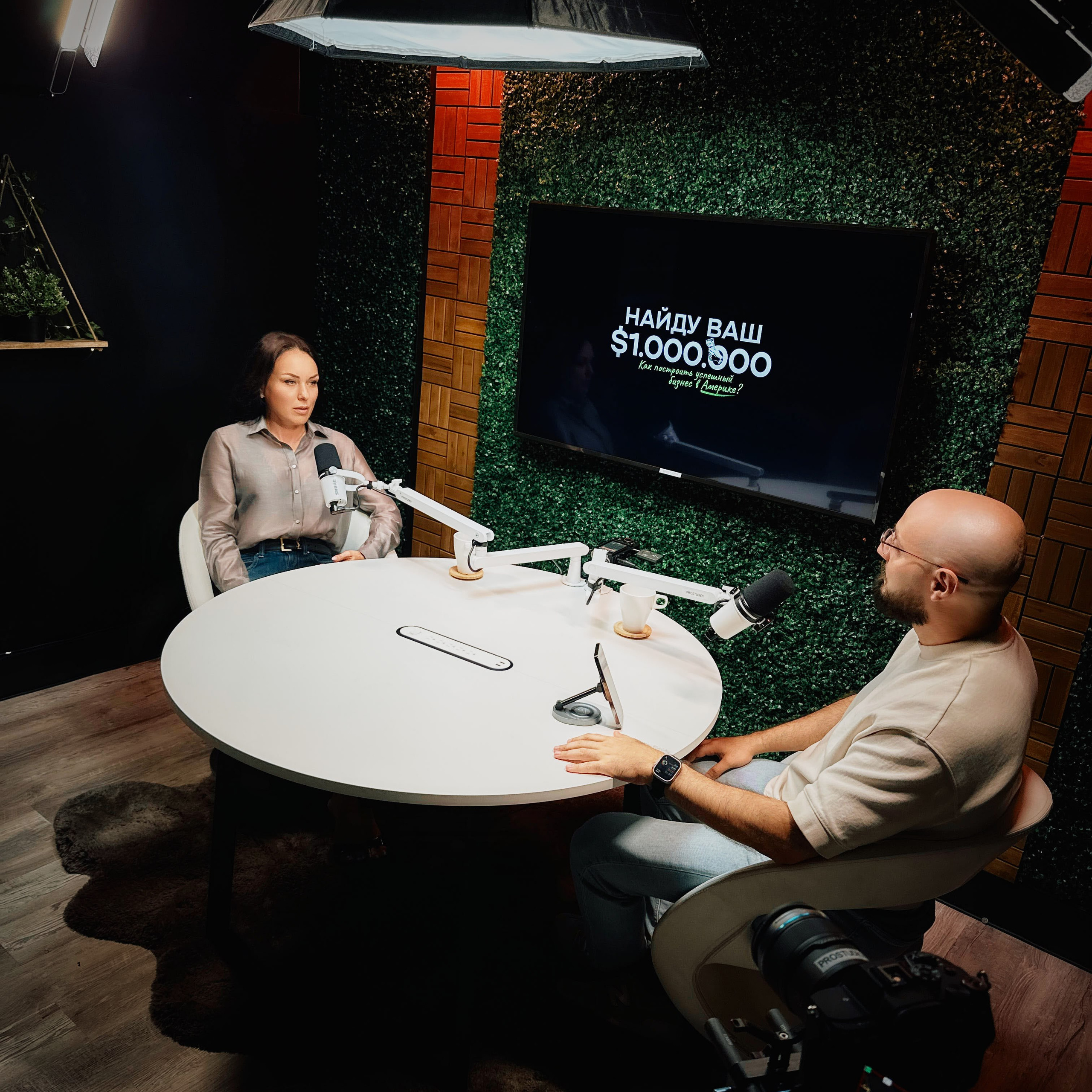 Wide shot of talk-show podcast set at ProStudio1 in Hollywood, FL — two guests at a round table with studio microphones and overhead light.