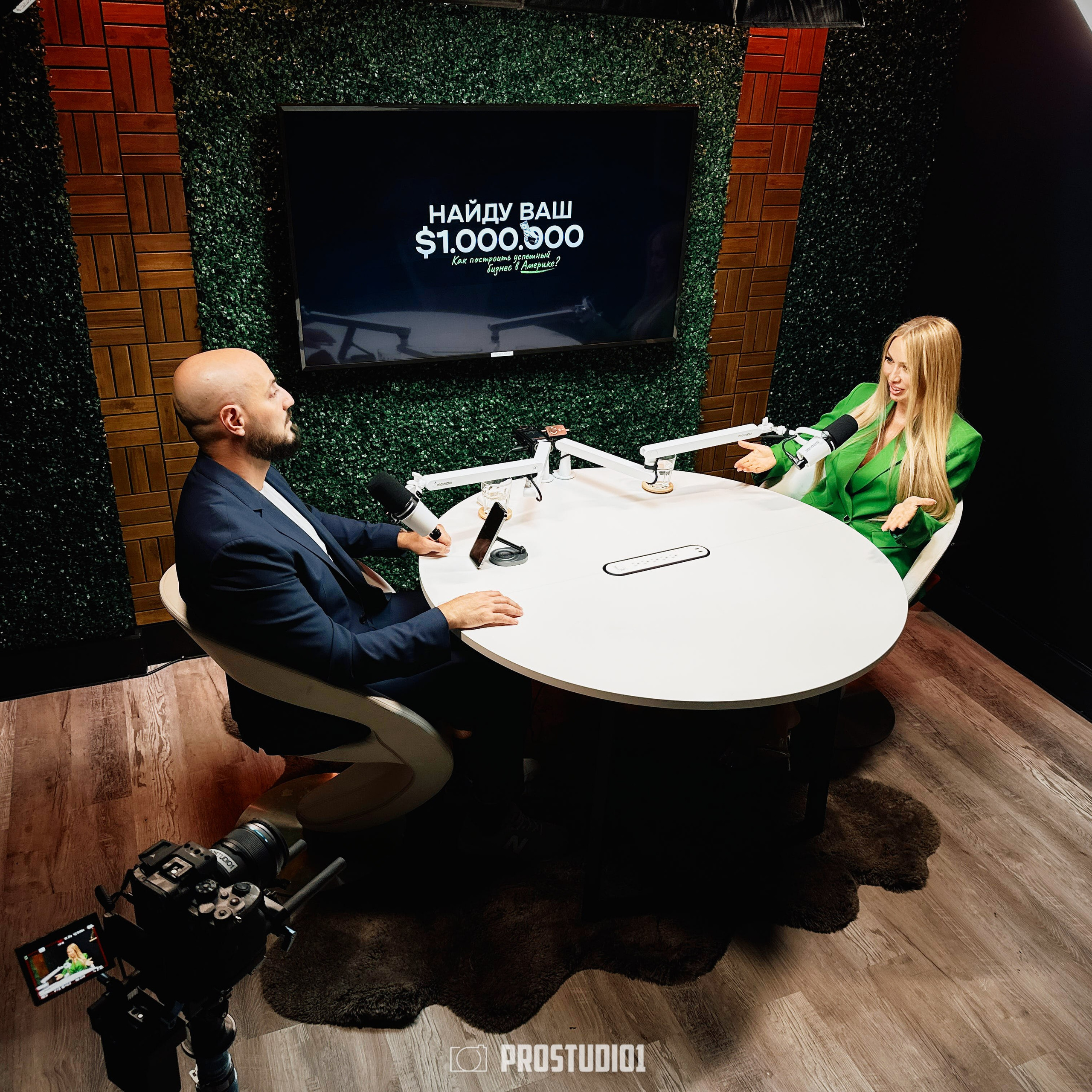 Top-down angle of podcast interview at ProStudio1, Hollywood FL — two guests seated at round table with microphones and cinematic lighting.