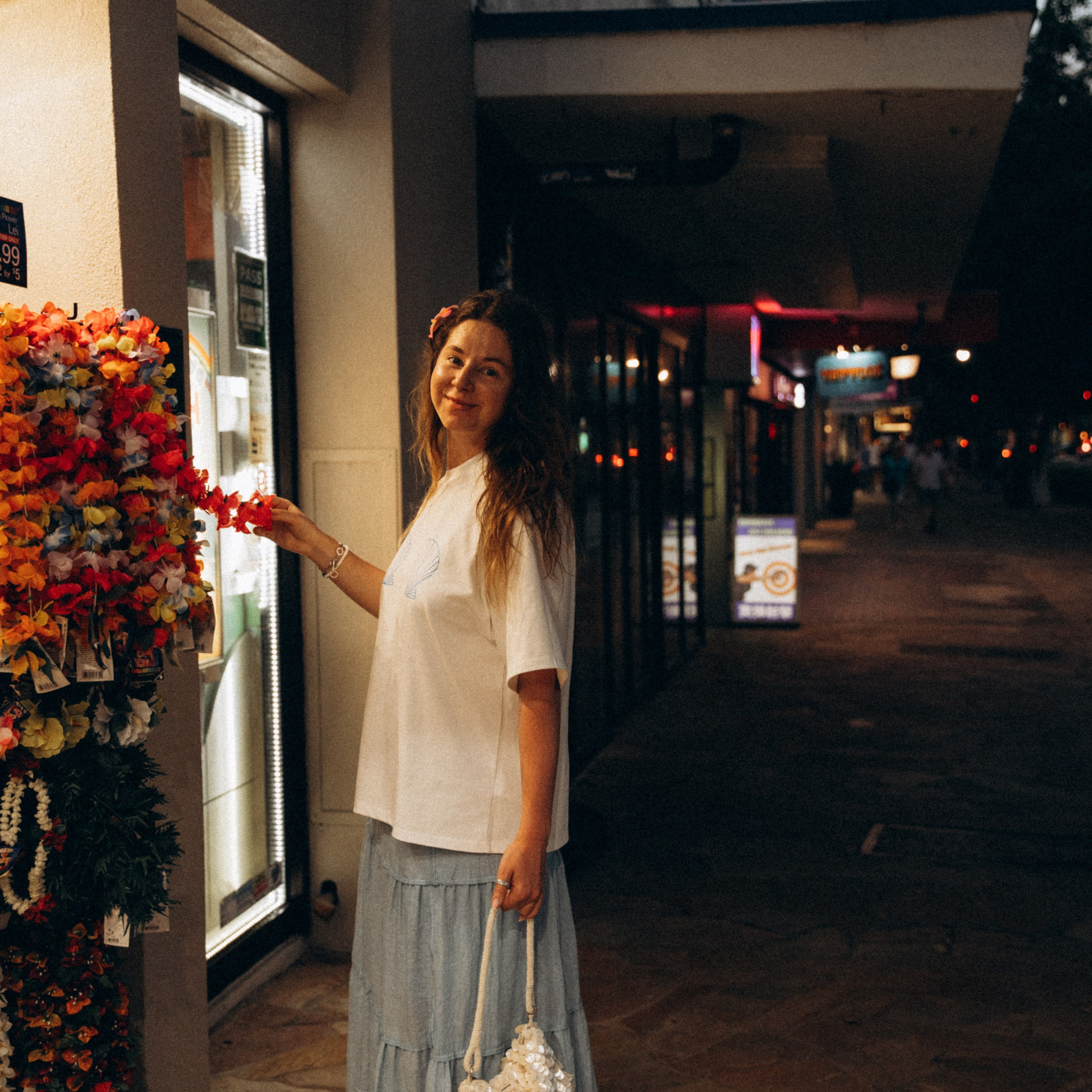 A girl choosing Hawaiian leis at a Waikiki souvenir shop at night