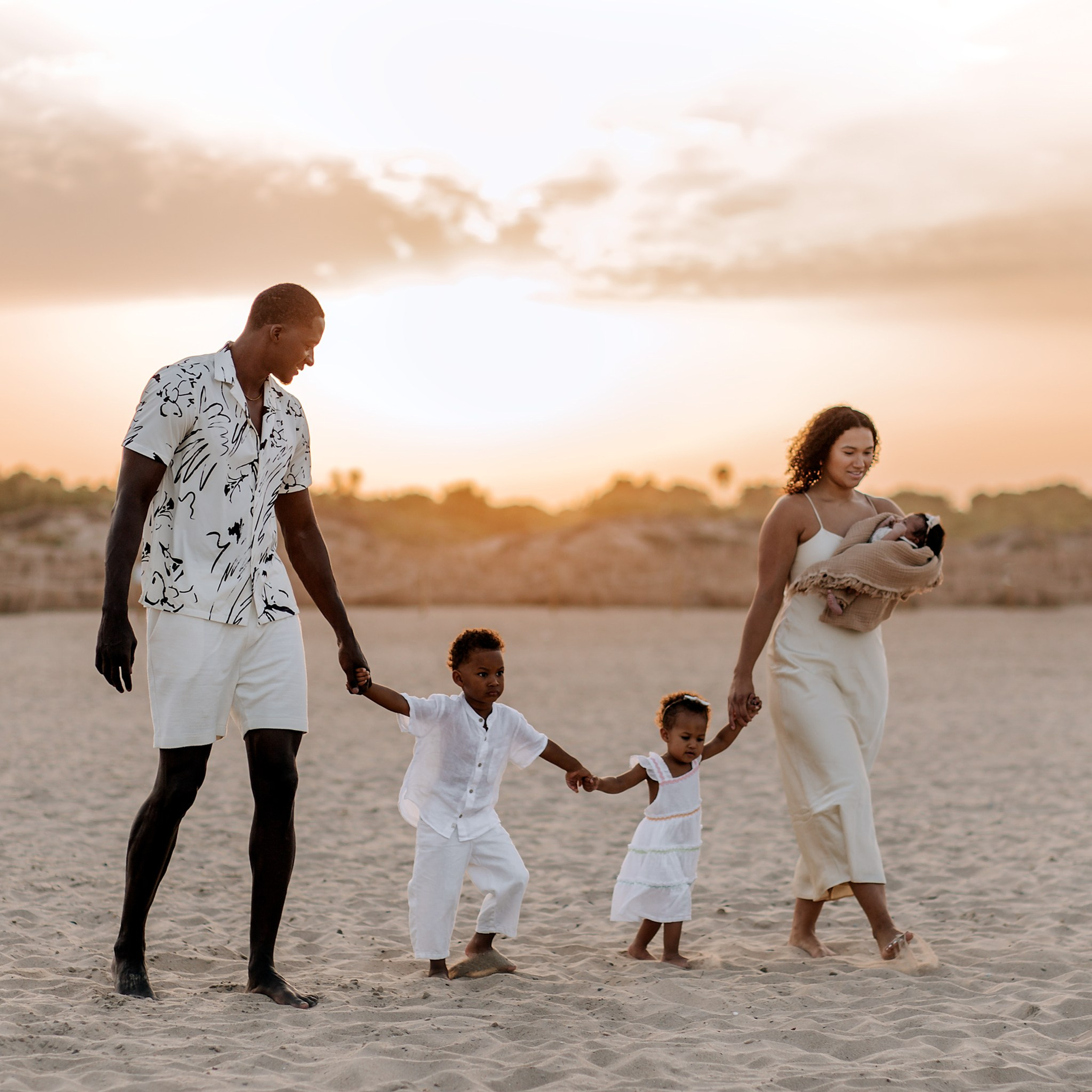 Sunset family beach photoshoot with African-American couple, their children, and a newborn walking hand-in-hand in Valencia, Spain