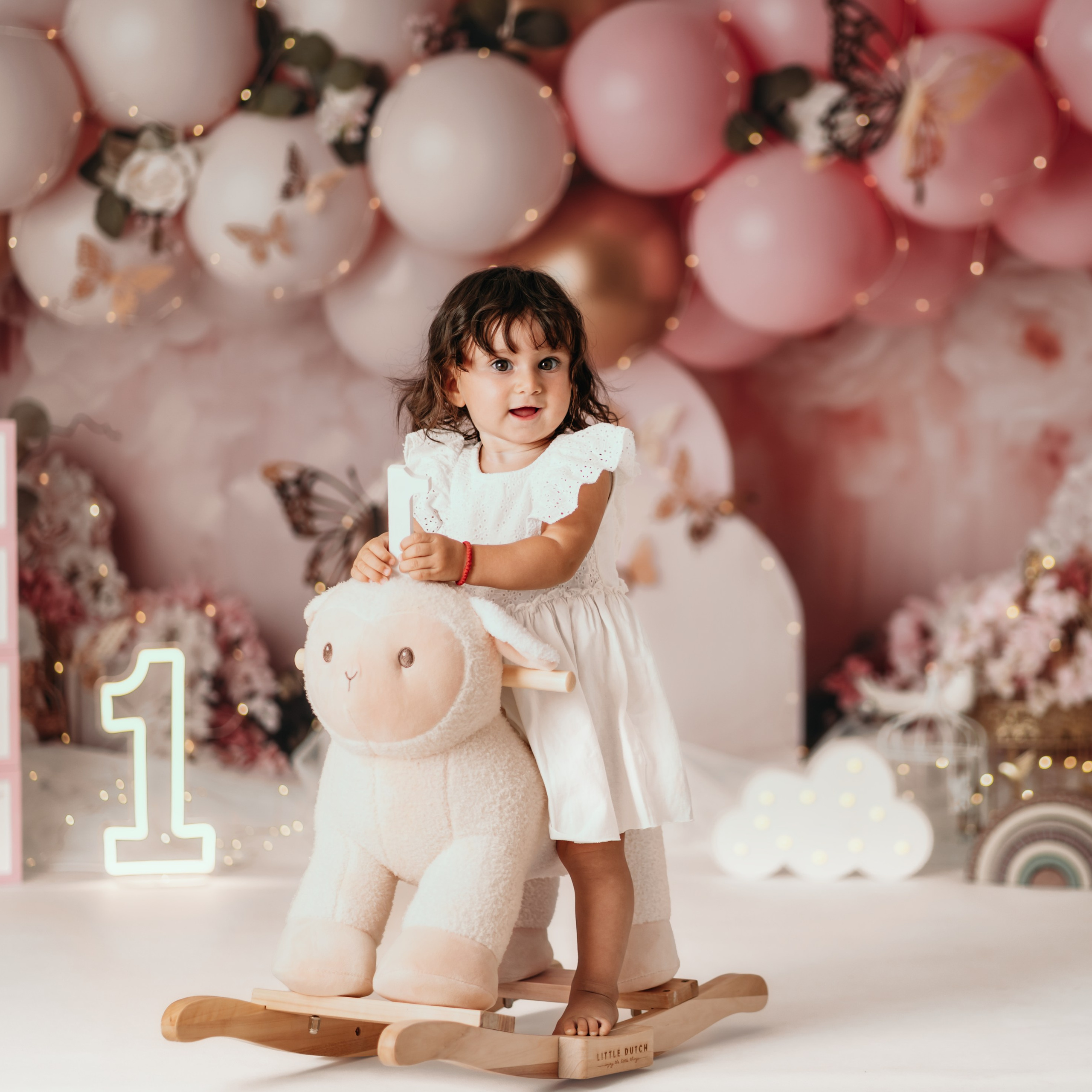 Cake smash Beograd – devojčica sedi na ljuljaški u obliku ovce u roze scenografiji