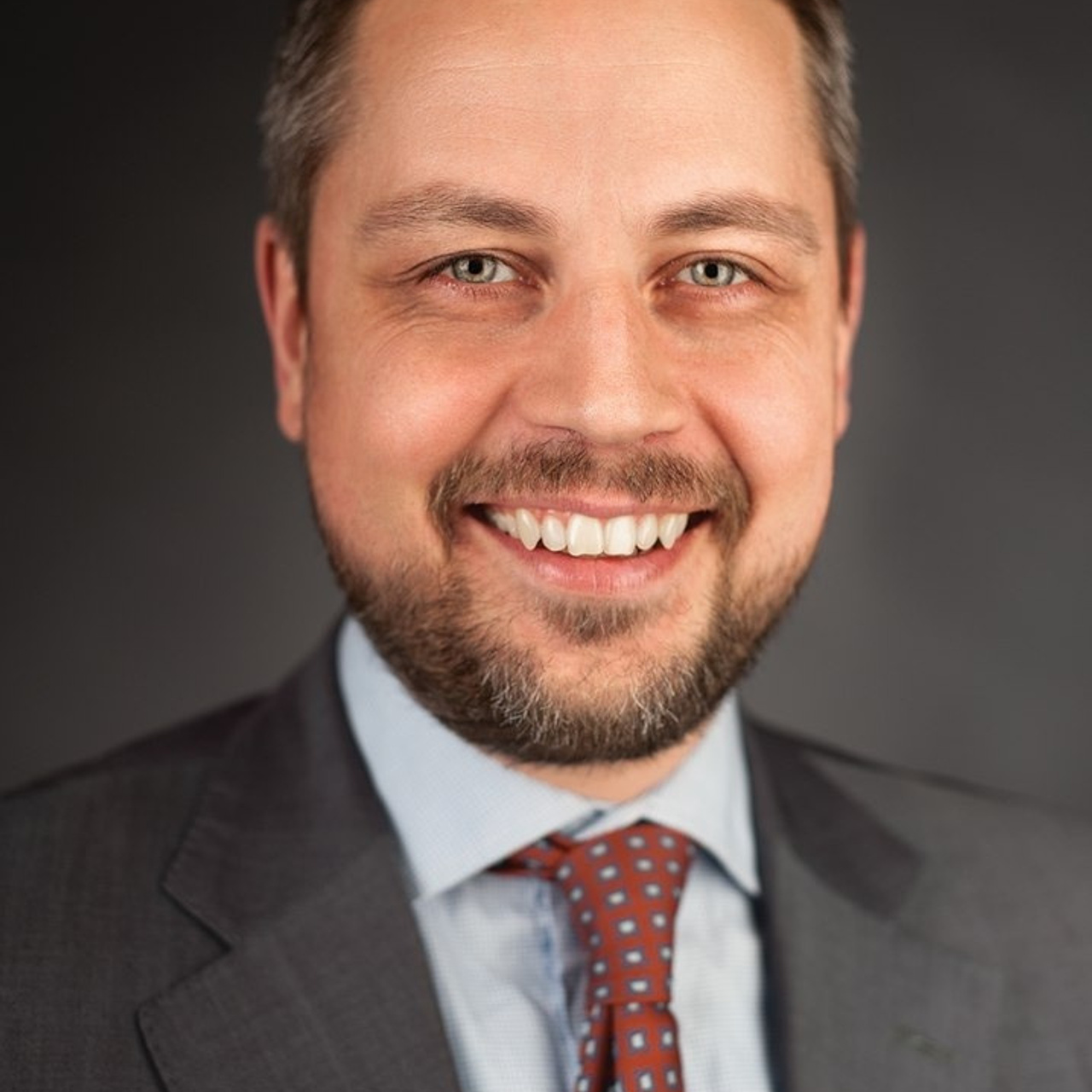 Close-up portrait of a business executive with a friendly smile, wearing a smart suit and patterned tie, taken by Dmitrii Shmatov for professional branding.