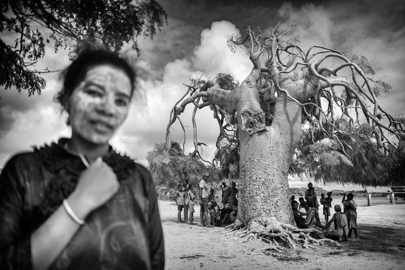 Clay mask and villagers sheltering under a tree to protect themselves from the sun, Ambazoa, Ambovombe district, Androy region, Toliara province, Republic of Madagascar. 2021