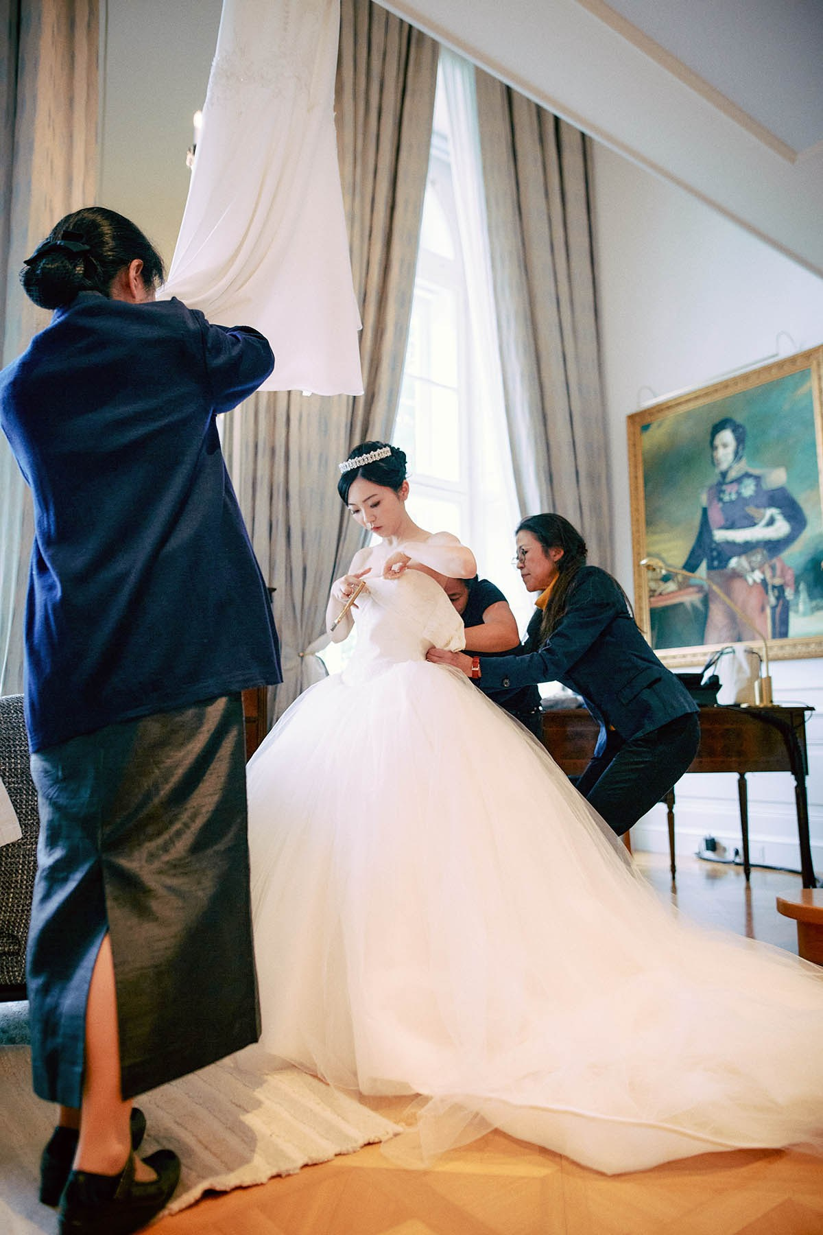 With the help of two assistants the bride is squeezed into her designer gown.