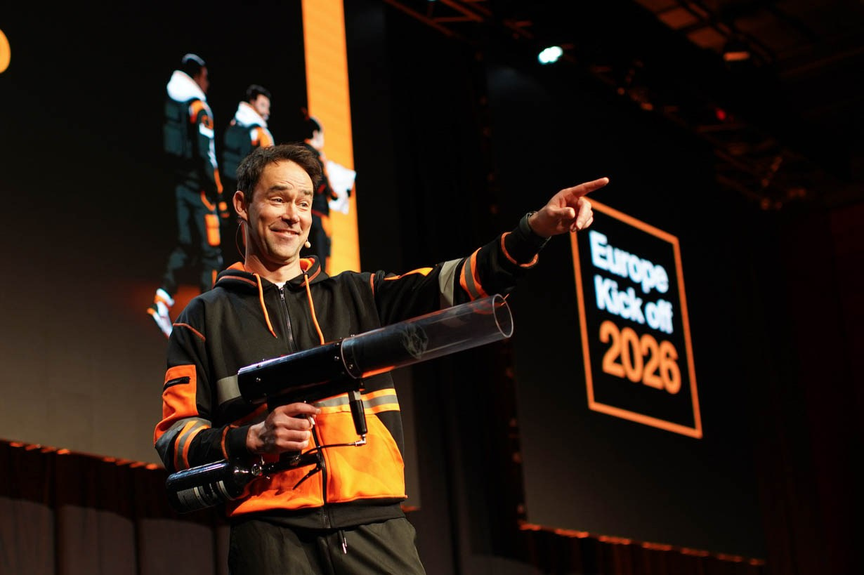 Emcee in black and orange attire opens the stage at Orange Business European Sales Kick-Off 2026 corporate event, Hilton Prague conference photography.