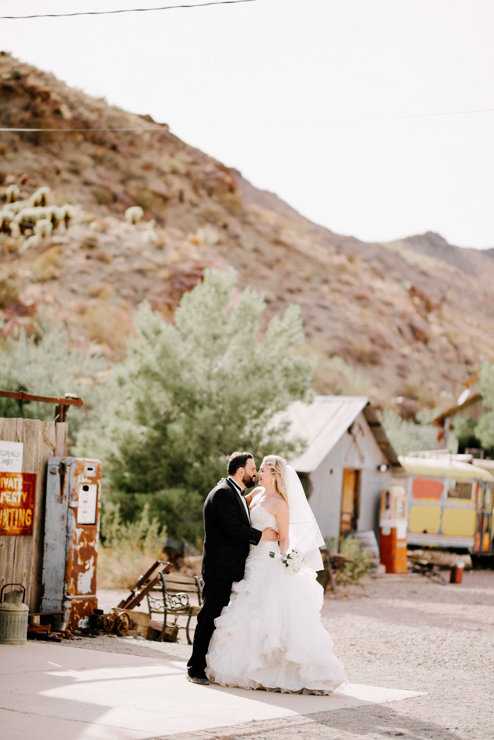 The bride and groom kiss against the backdrop of mountains and an abandoned parking lot.