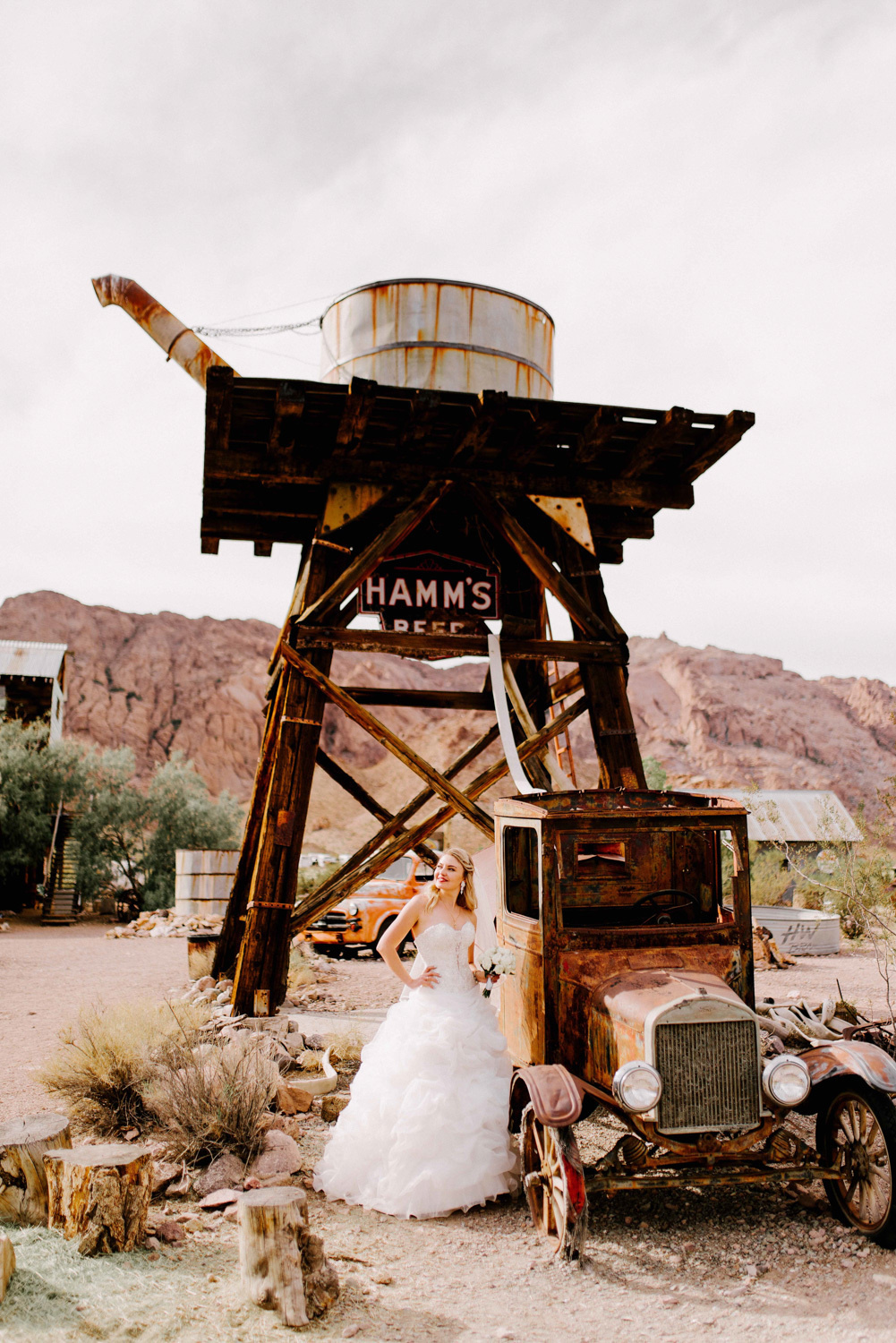 Bride at an old truck near a tower with a barrel on the background of mountains.