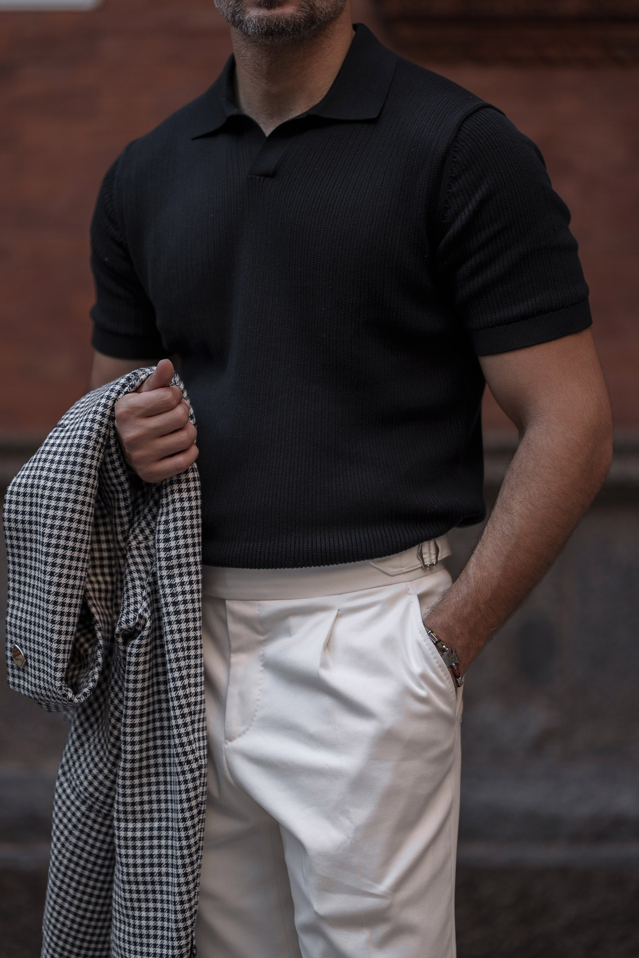 Detail of a black polo shirt, white trousers and checked blazer