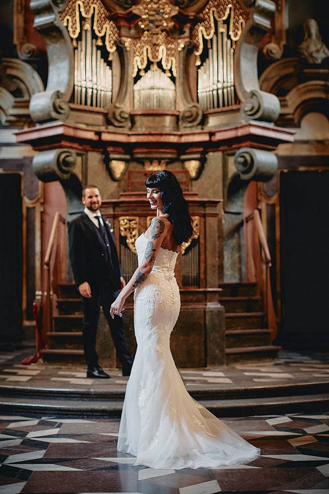 Tattooed bride confident pose with admiring groom at the chapel altar.