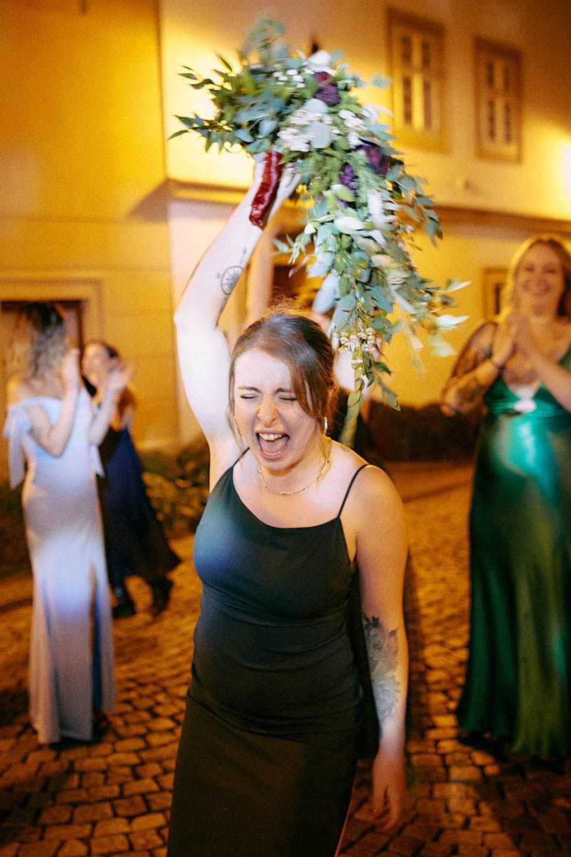 Ecstatic guest screaming joyfully, holding a caught bouquet aloft.
