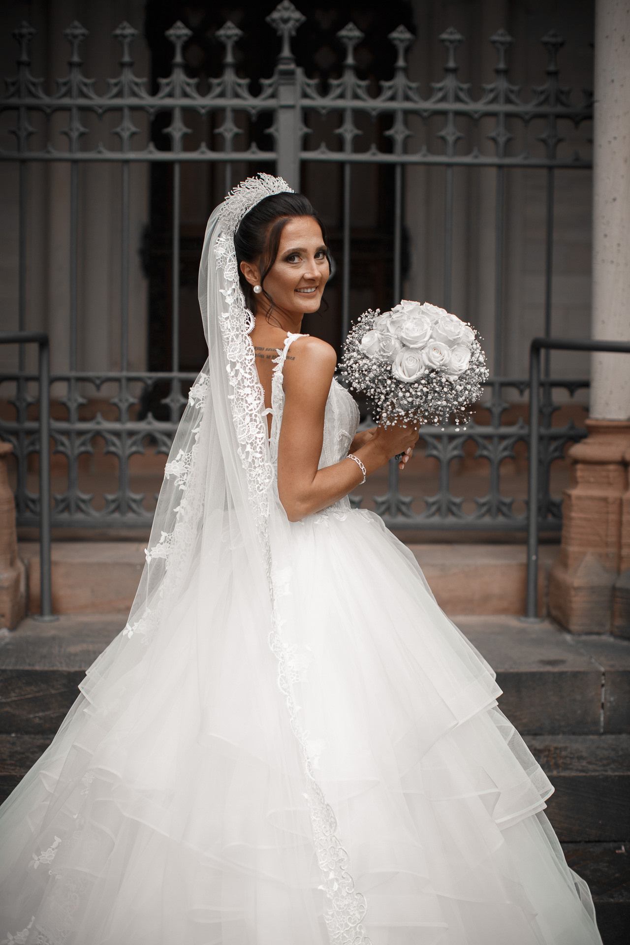 Die Braut lächelt verträumt und hält ein Bouquet aus Blumen in den Händen.