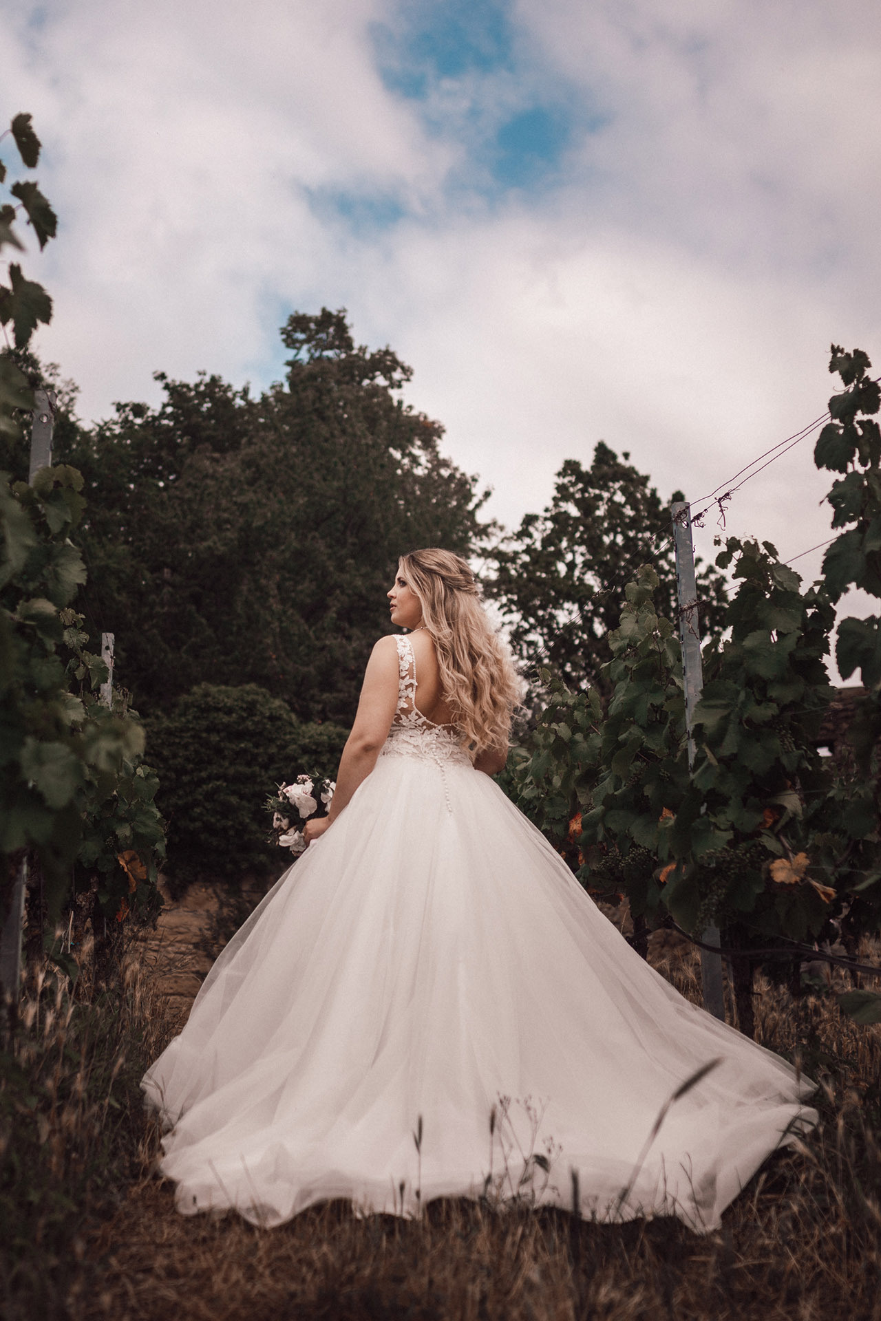 Braut in traumhaftem Hochzeitskleid läuft durch Weinberge – stilvolle Hochzeitsfotografie
