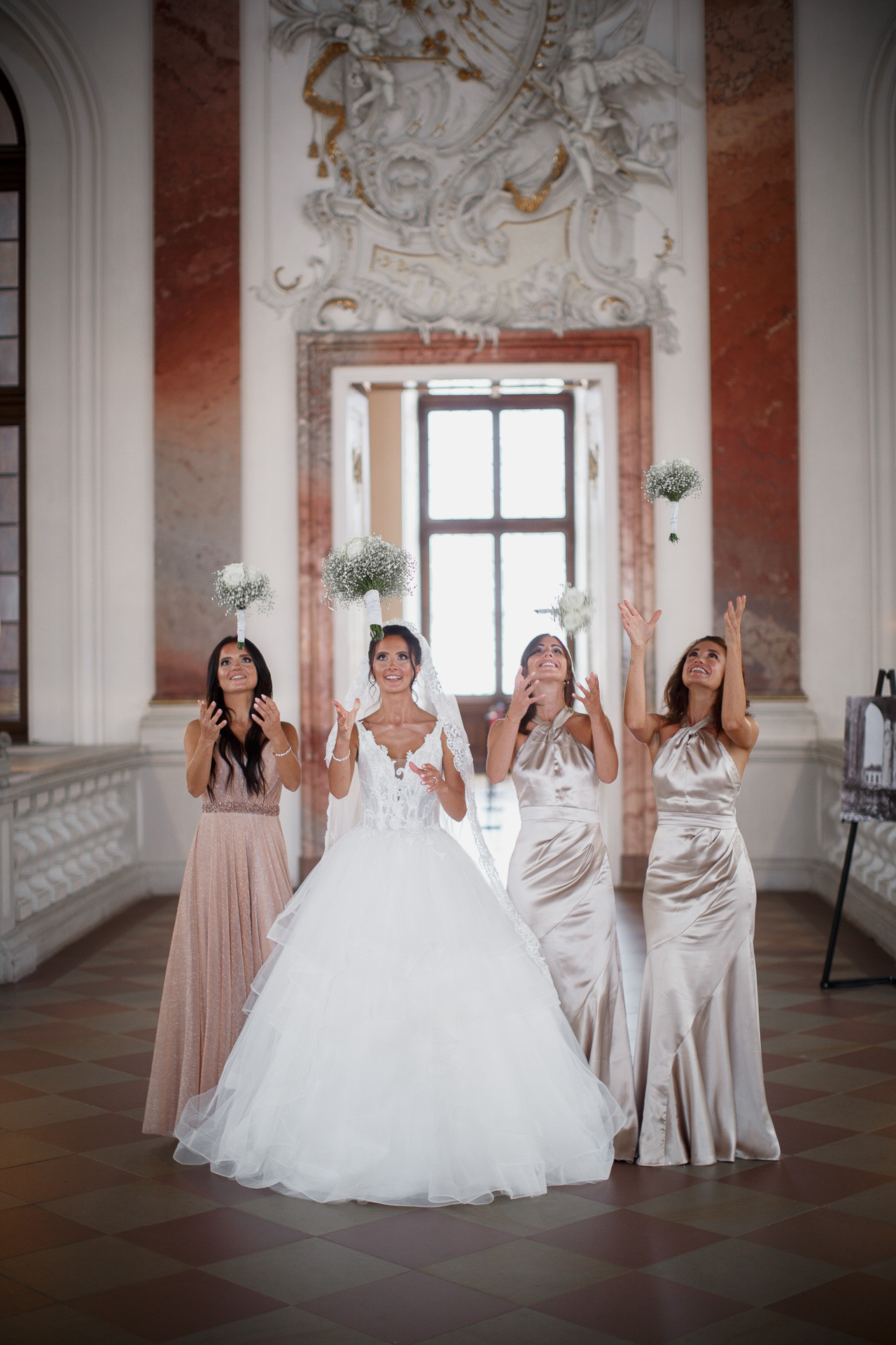 Die Braut und ihre Brautjungfern werfen begeistert Blütenblätter in die Luft vor der majestätischen Schlosskulisse.