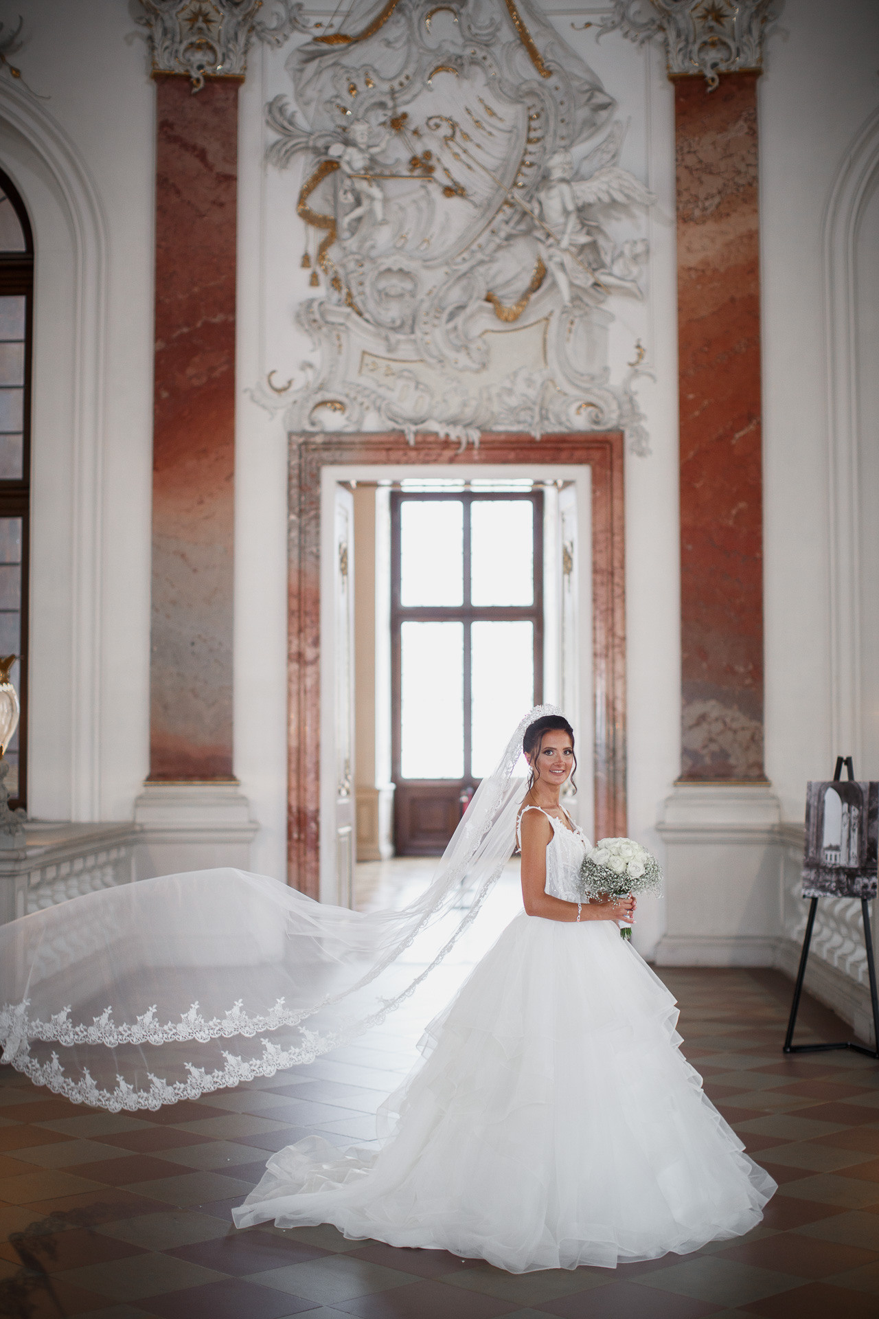 Die Braut lässt ihren Brautschleier im Wind vor der Schlosskulisse wehen