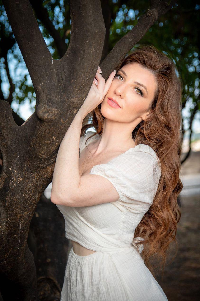 a woman with wavy hairstyle and romantic makeup posing next to a tree