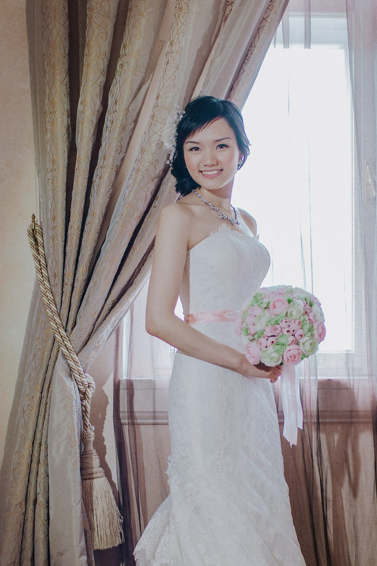 A bridal portrait of the smiling Hong Kong bride as she poses with her bouquet in her luxury suite in Prague.