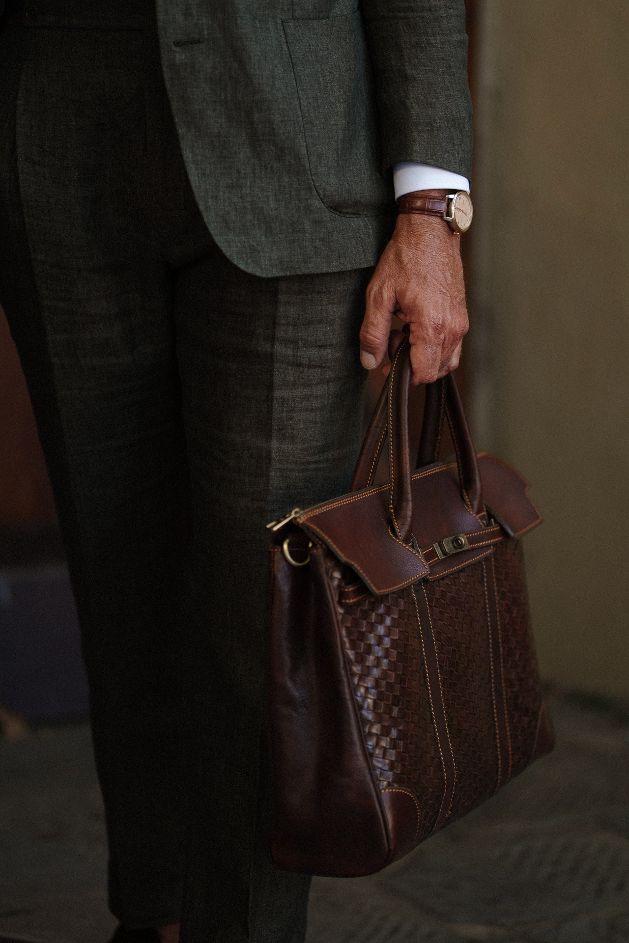 Dettaglio fotografico da Pitti Uomo 110, borsa in pelle marrone e pantaloni sartoriali grigi