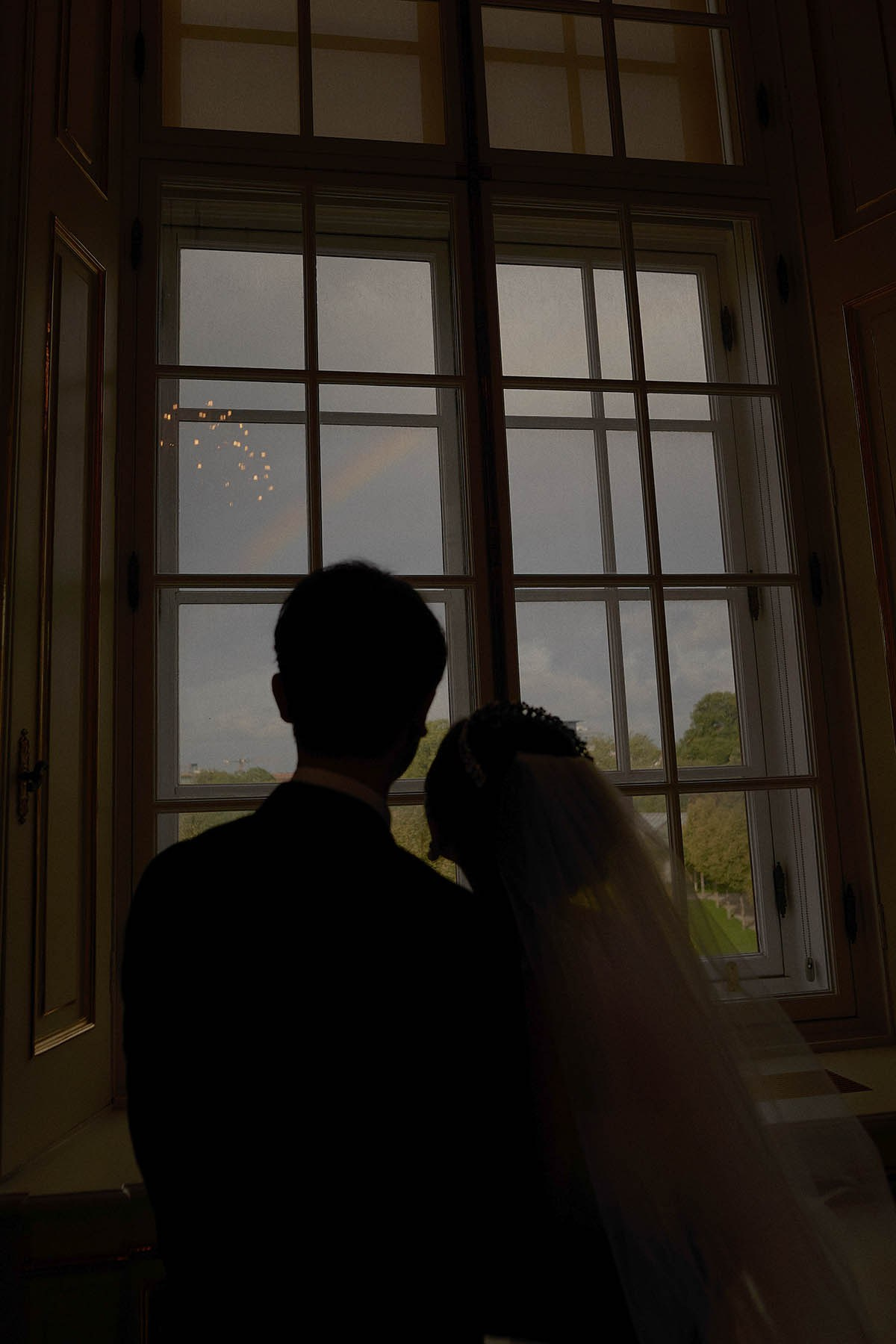 Newlyweds silhouetted with rainbow through windows at Belvedere Palace.