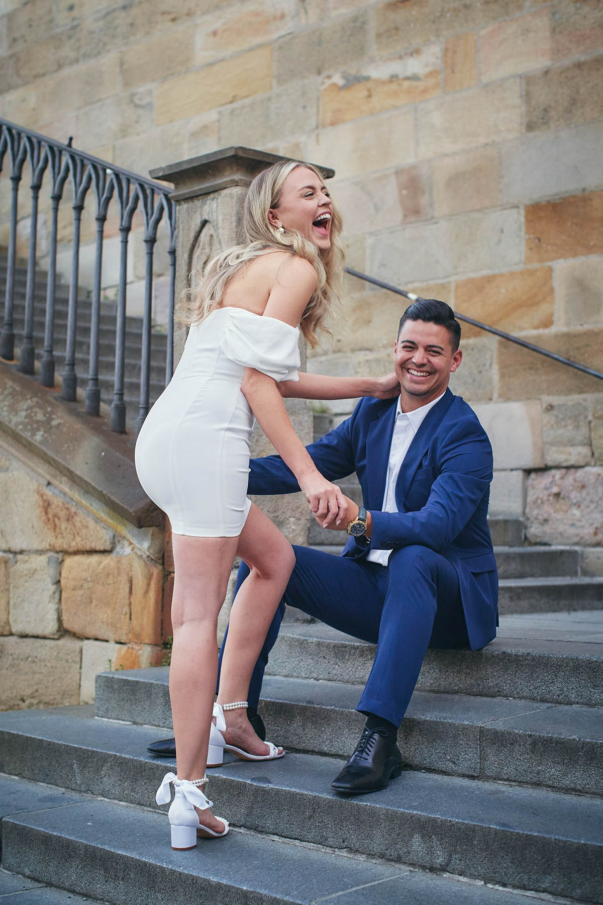 Flirty Southern California couple posing on historic Kampa Steps during dreamy sunrise engagement.