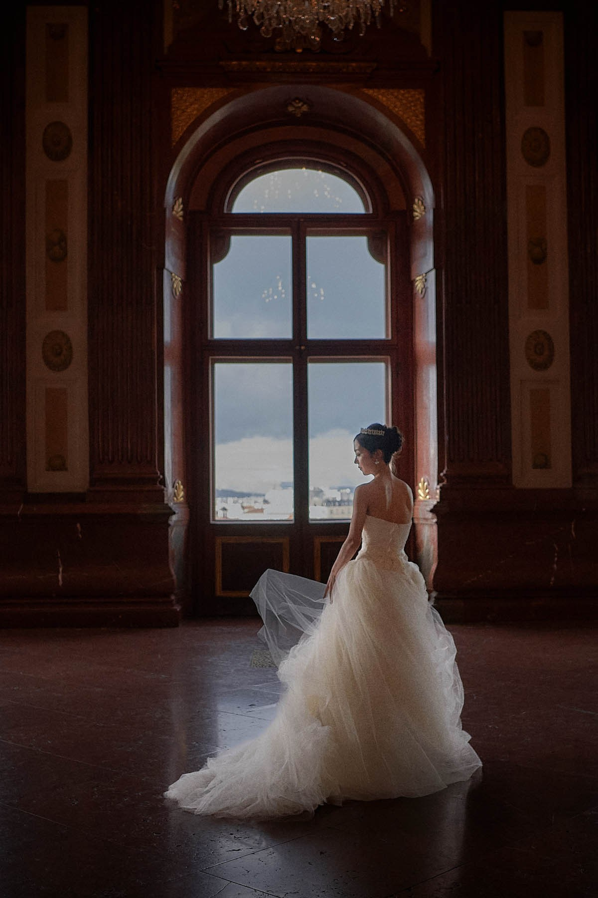 Bride adjusting wedding dress silhouetted in Belvedere Palace hall.