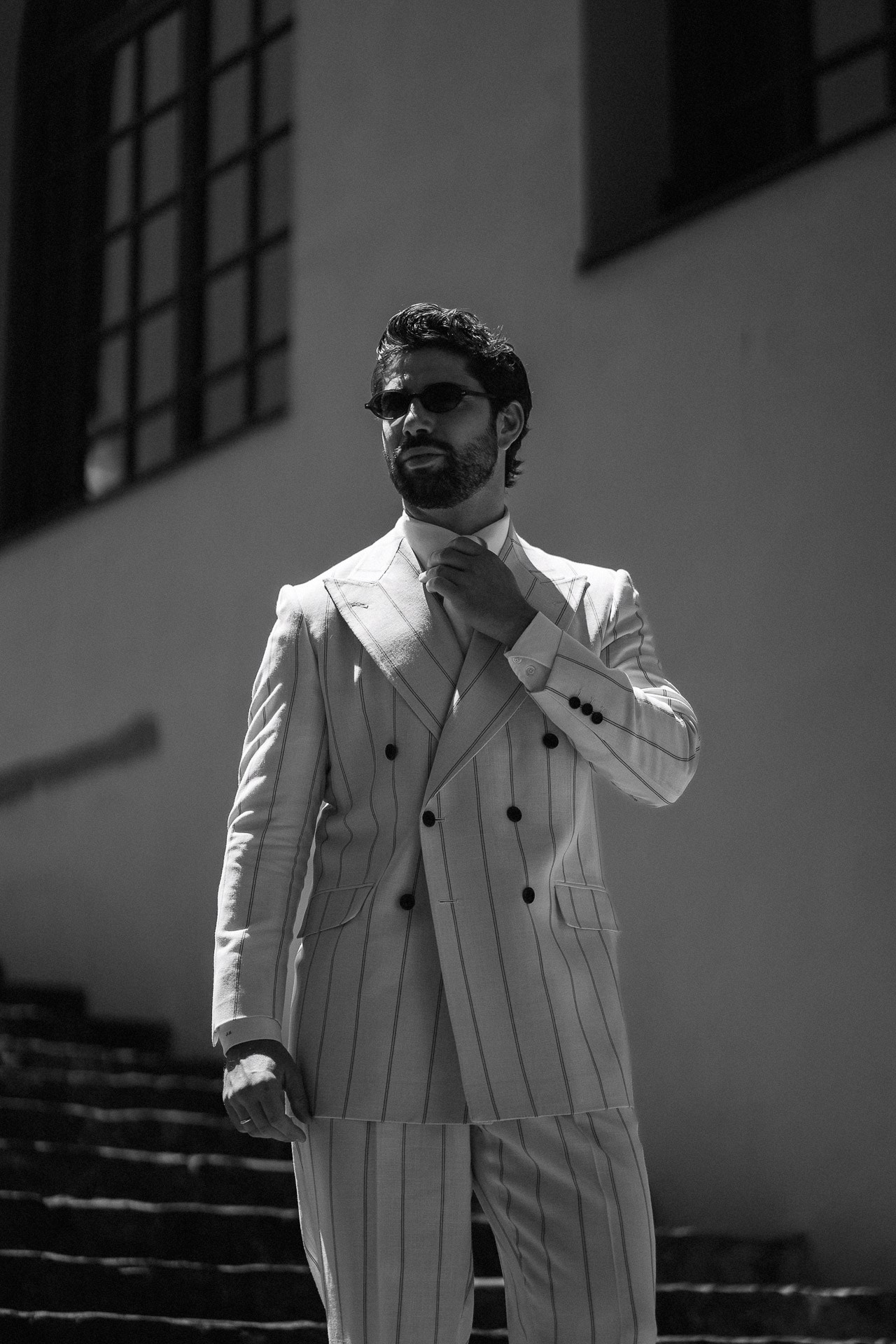 Ritratto in bianco e nero da Pitti Uomo 110, uomo in completo doppiopetto bianco gessato sulle scale