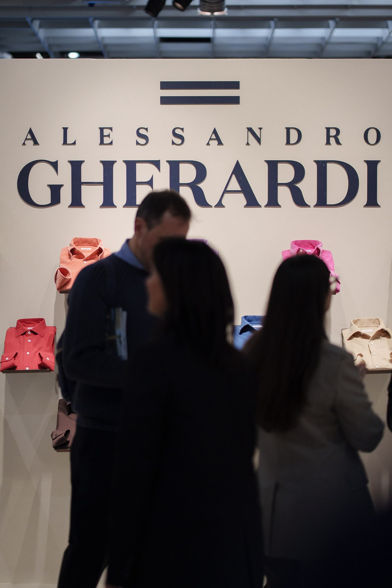 Visitors exploring the Alessandro Gherardi stand at Pitti Uomo, with colorful shirts displayed in the background.