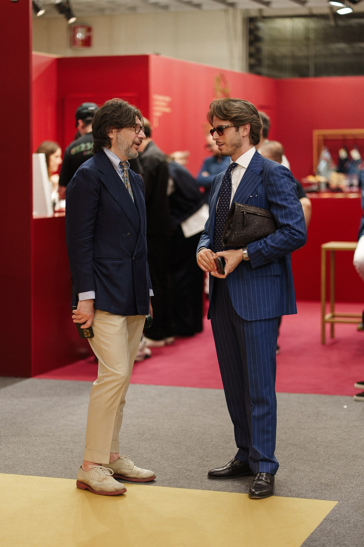 Scena street style da Pitti Uomo 110, due ospiti in completi sartoriali blu che parlano dentro la fiera