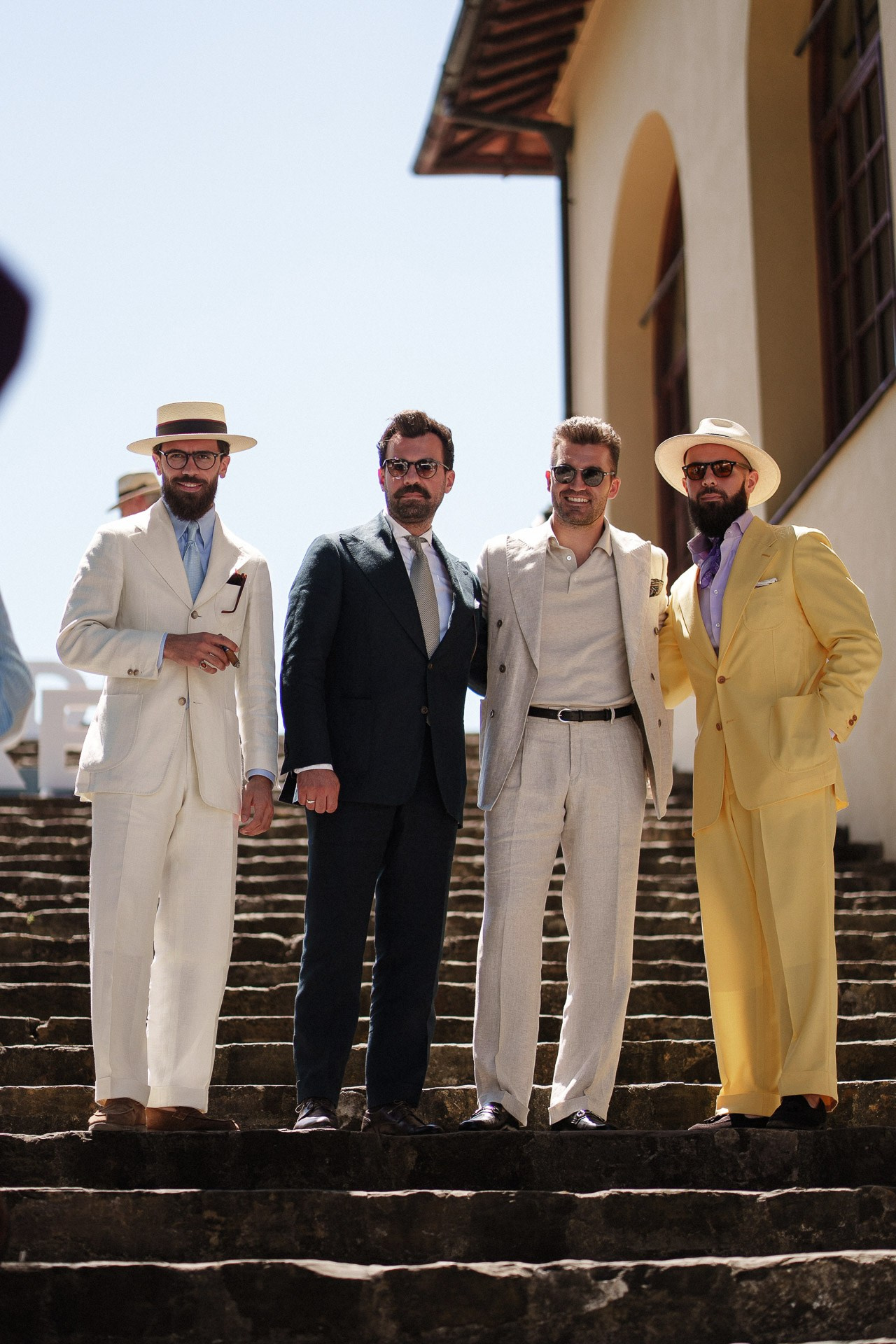 Ritratto di gruppo da Pitti Uomo 110, quattro ospiti in classico tailoring estivo sulle scale a Firenze