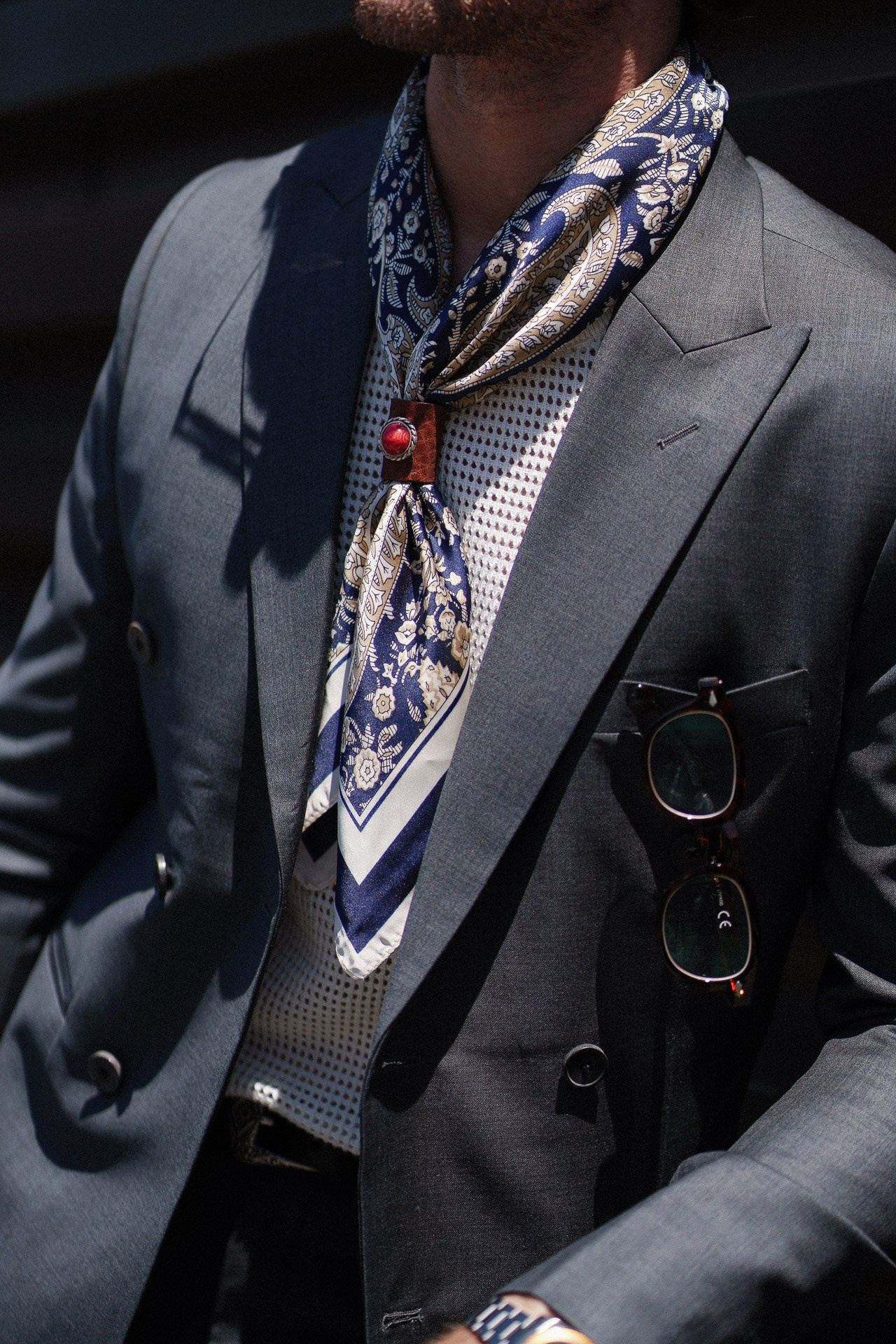 Dettaglio da Pitti Uomo 110, blazer grigio scuro con foulard di seta fantasia e occhiali da sole
