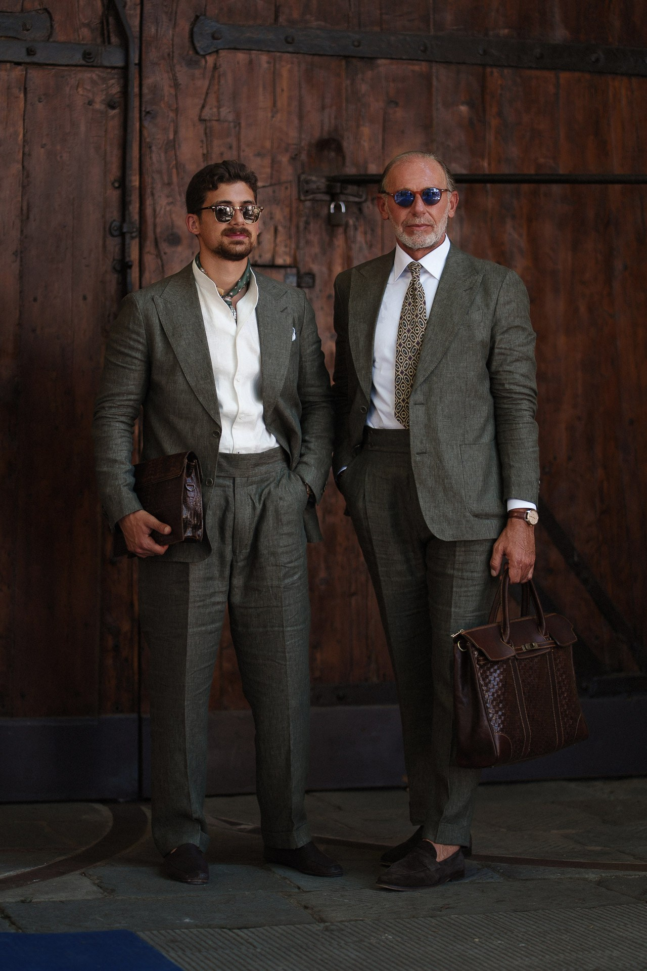 Ritratto street style da Pitti Uomo 110, due ospiti in completi grigio e verde davanti a porte in legno