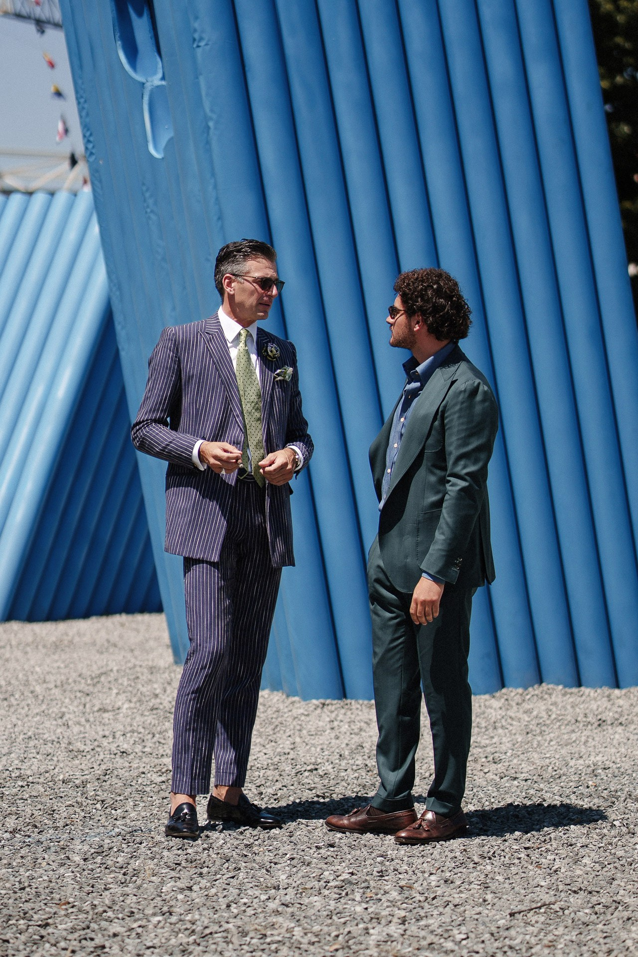 Scena street style a Pitti Uomo 110, due ospiti in completi sartoriali che parlano vicino all’installazione blu