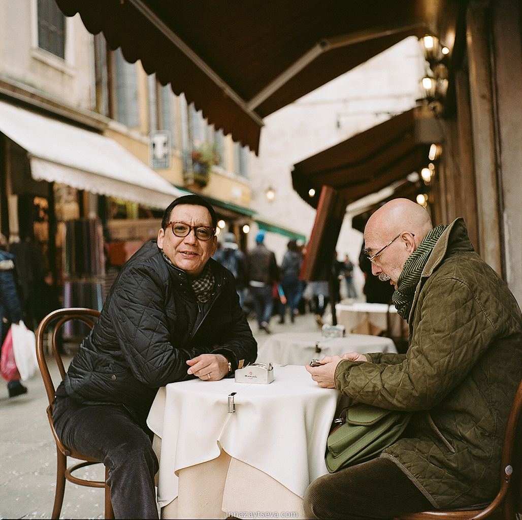 Egor Konchalovsky and  Andrey Bildgo during Venice Carnaval sitting and talking  at the table in Italy
