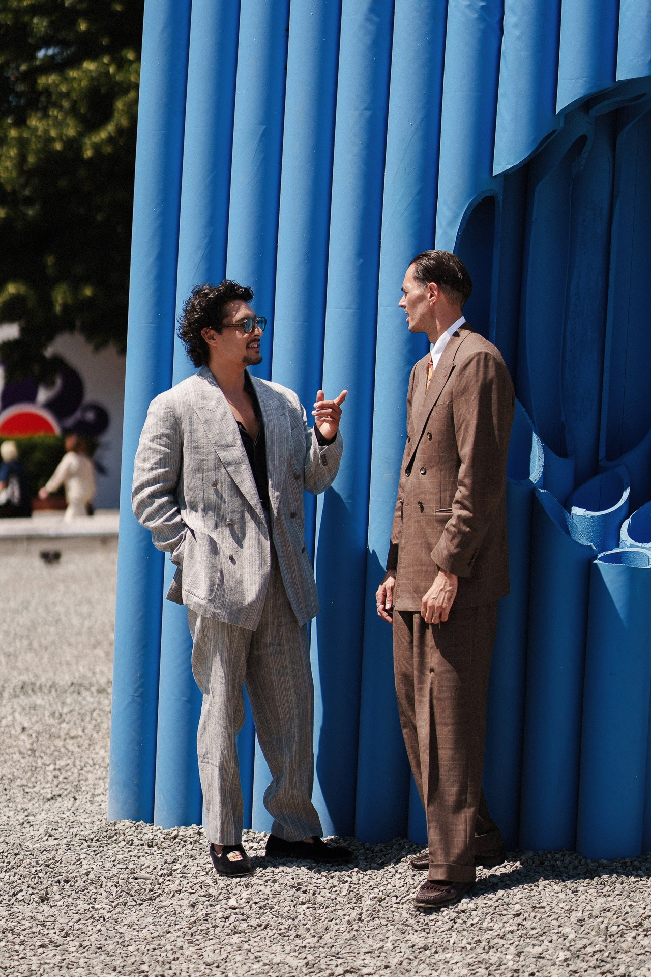 Scena street style a Pitti Uomo 110, due ospiti che parlano vicino all’installazione blu a Firenze
