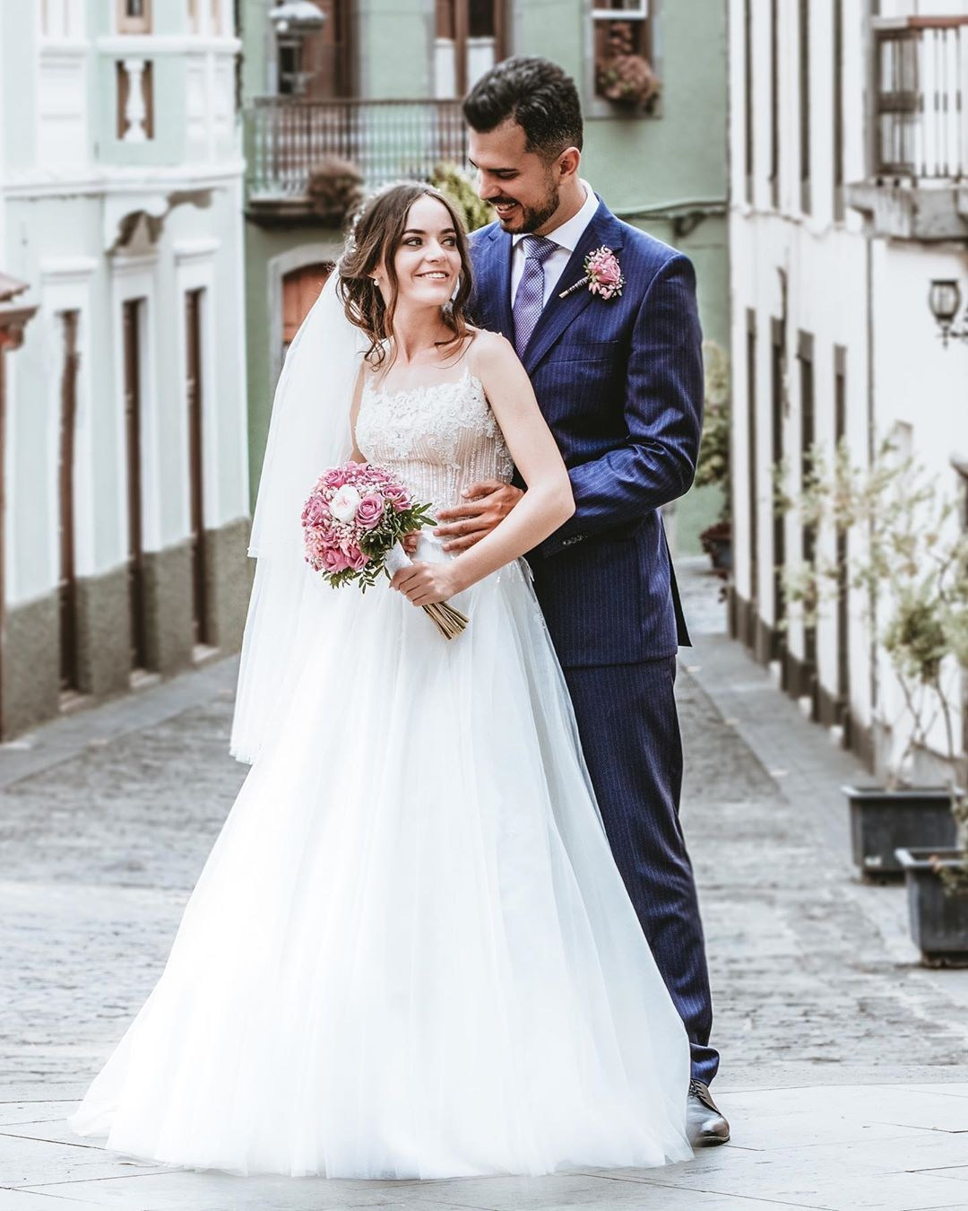 Une mariée et un marié s'embrassent dans une rue pavée.