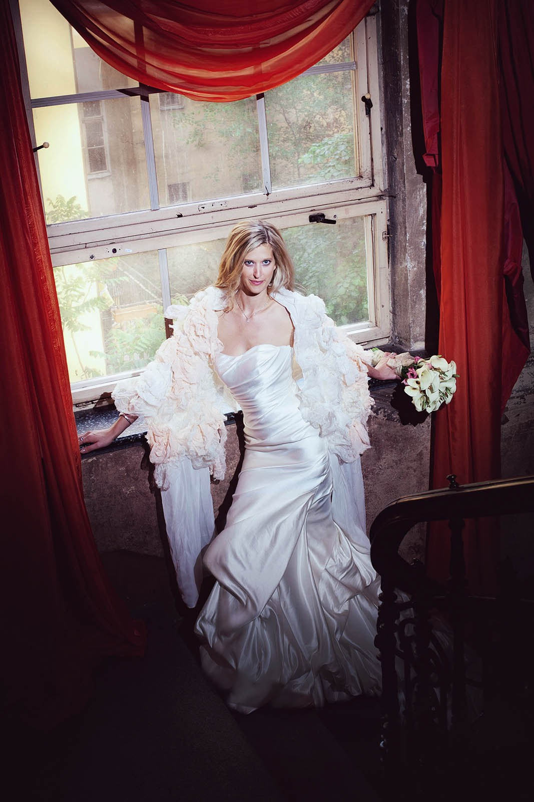 A beautiful blonde-haired bride poses surrounded by red fabric in Prague