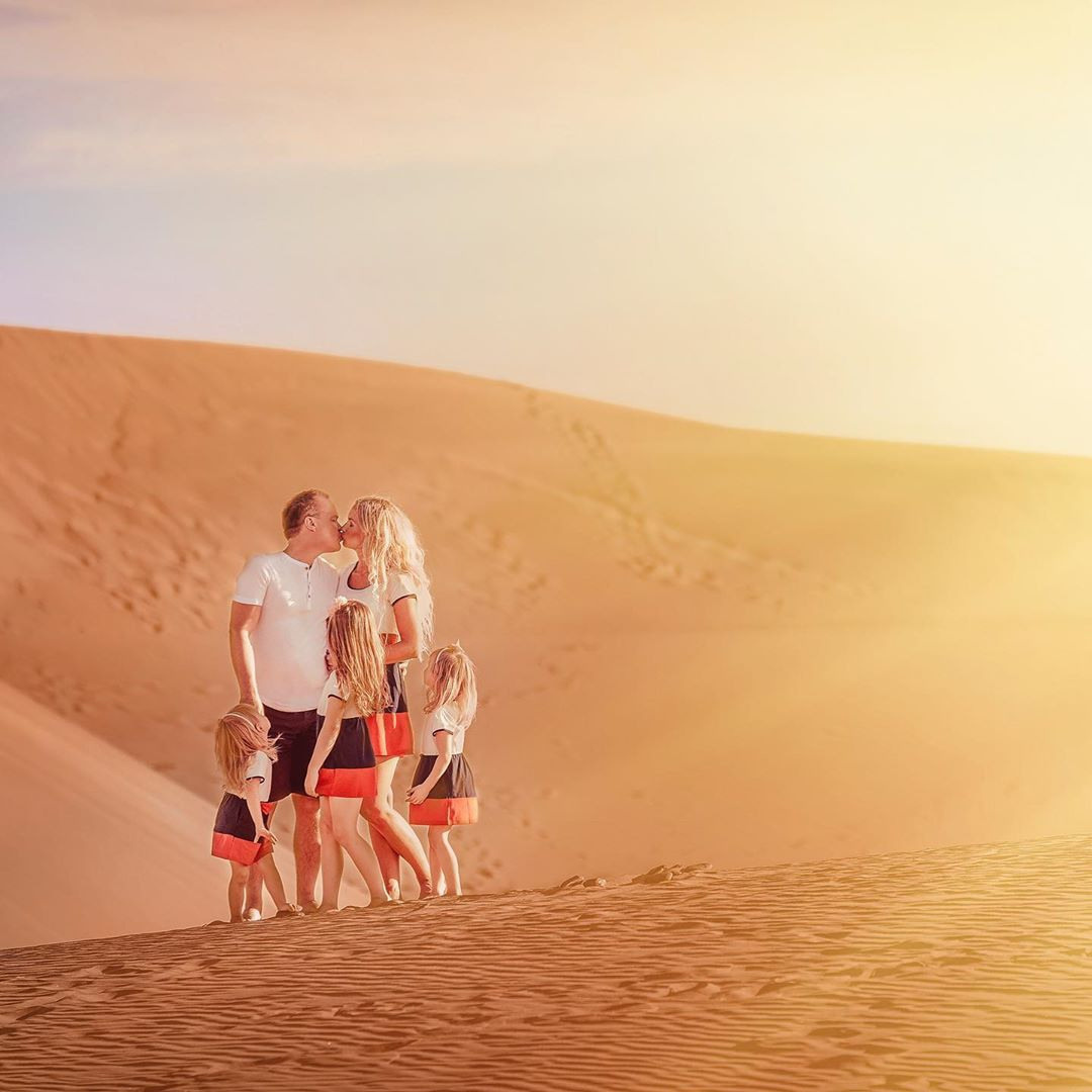 A family is standing on top of a sand dune at sunset.