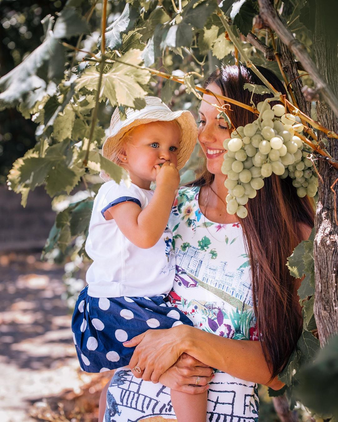 A woman and child are holding grapes in a vineyard.