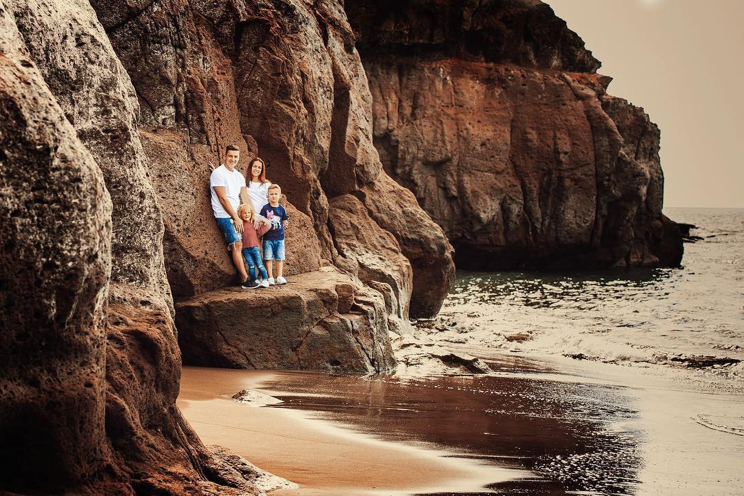 A couple is standing on a cliff near the ocean Taurito