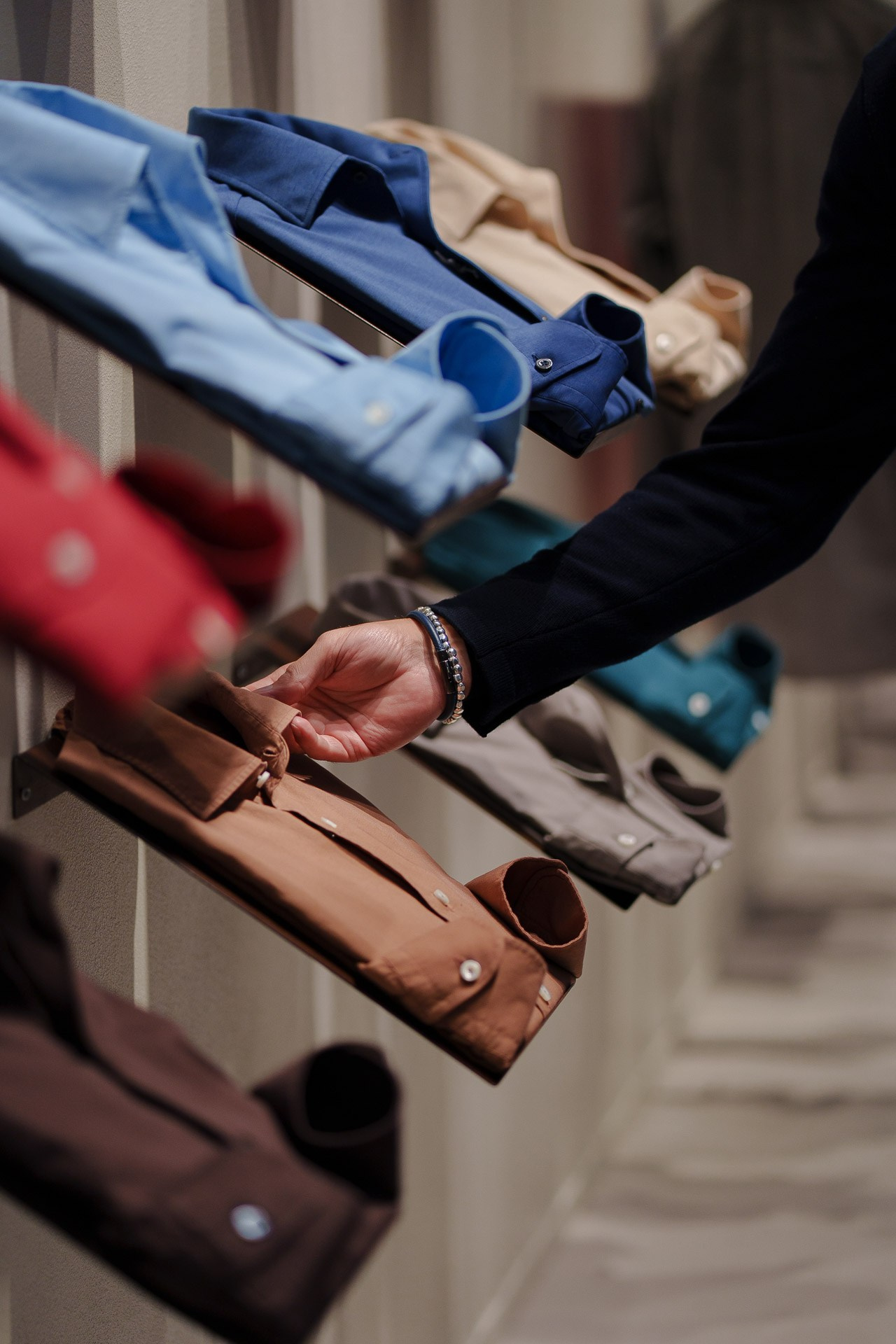 A person’s hand reaching for a tailored brown shirt from a professional showroom display at Pitti Uomo.