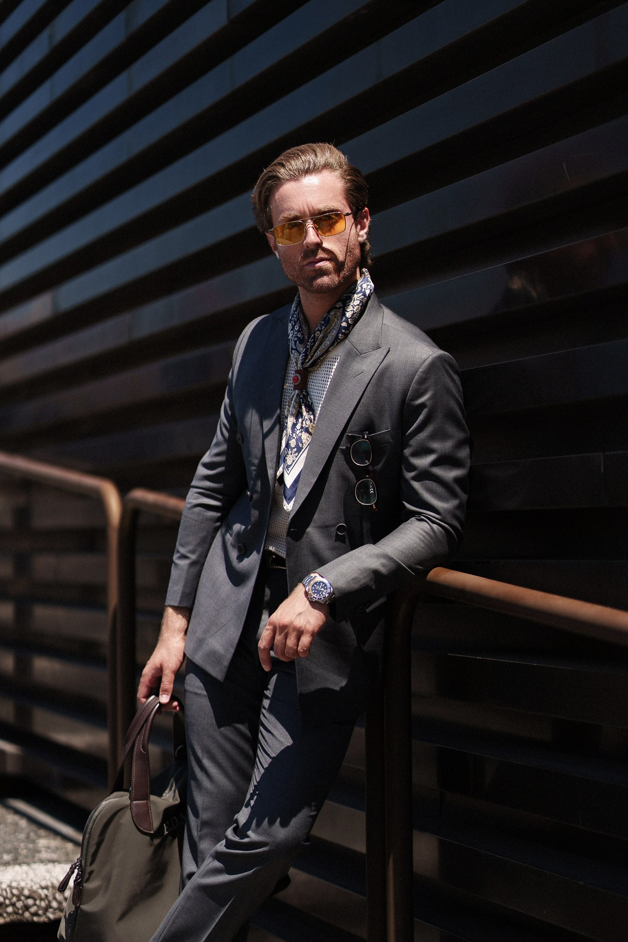 Ritratto street style da Pitti Uomo 110, uomo in completo grigio scuro con foulard fantasia e borsa in pelle a Firenze