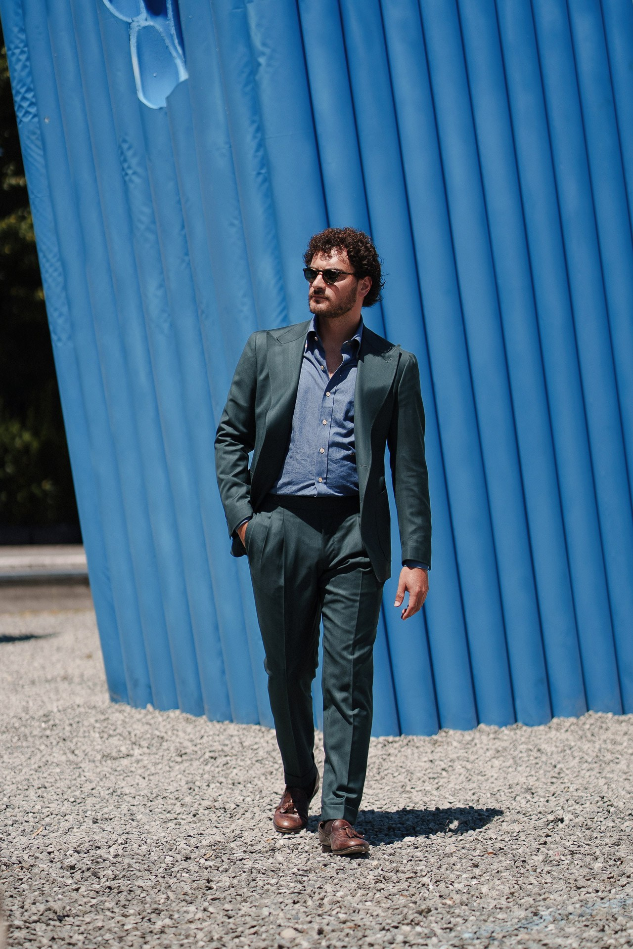 Ospite di Pitti Uomo 110 in completo verde che cammina accanto all’installazione blu alla Fortezza da Basso