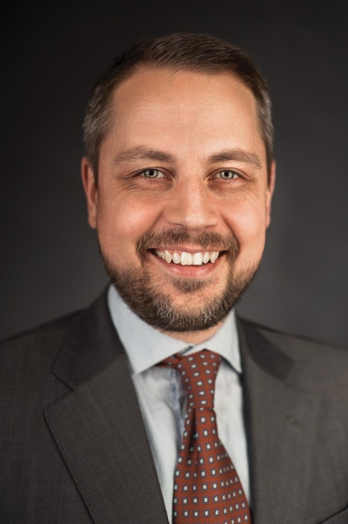 Close-up executive headshot of a smiling man in a grey suit, professional photography for LinkedIn and corporate use.