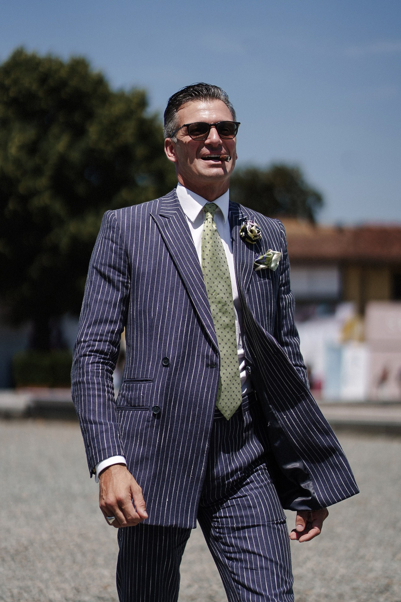 Ritratto street style da Pitti Uomo 110, uomo in completo gessato blu navy con cravatta verde e boutonniere