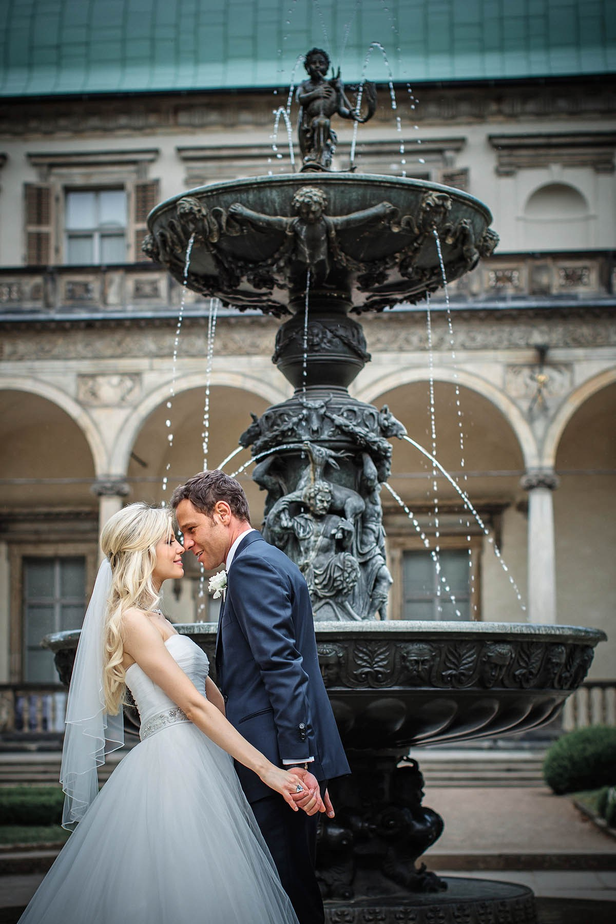 Newlyweds kissing hand-in-hand by fountain Belvedere Prague