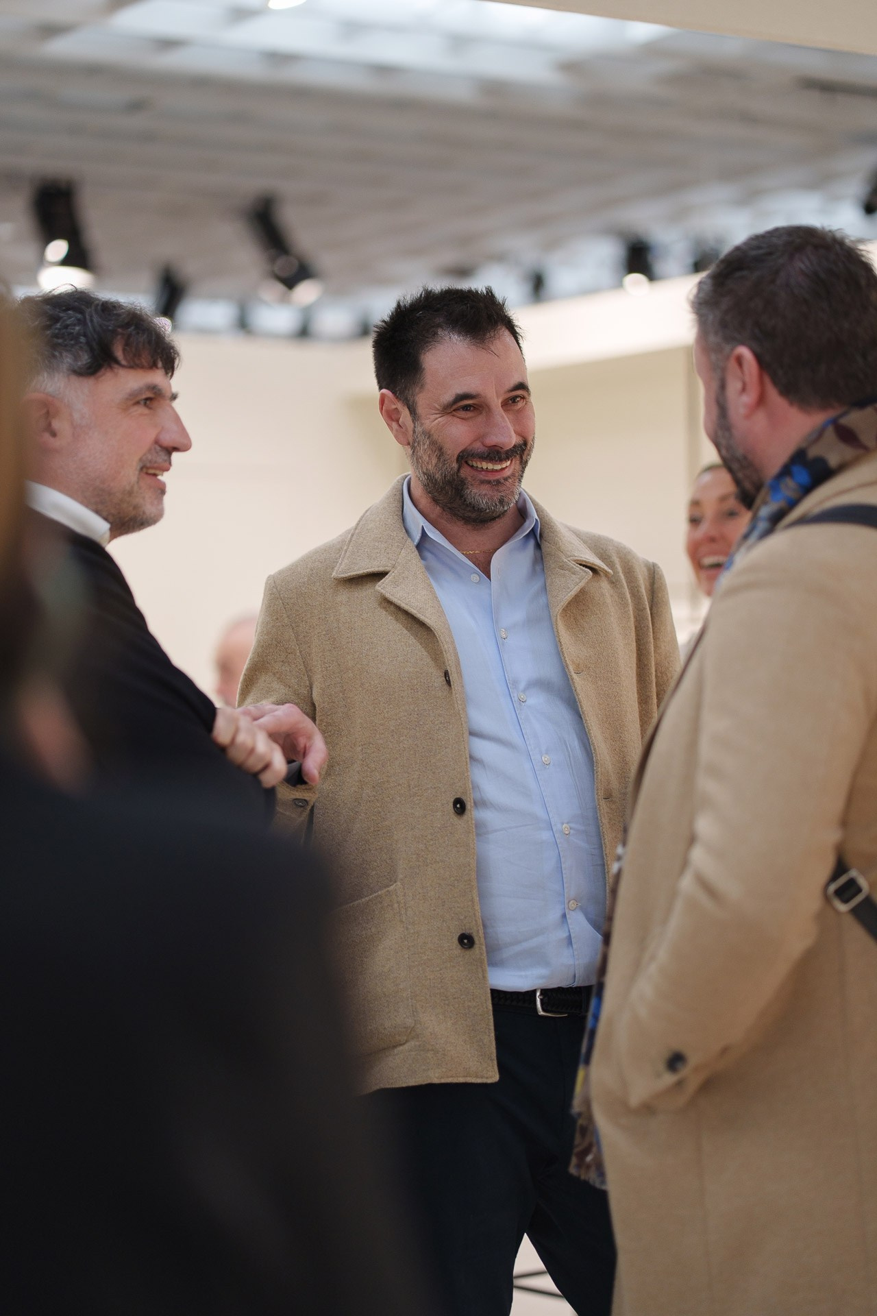 Stylish men in camel coats and light blue shirts networking during the world's leading menswear trade show.