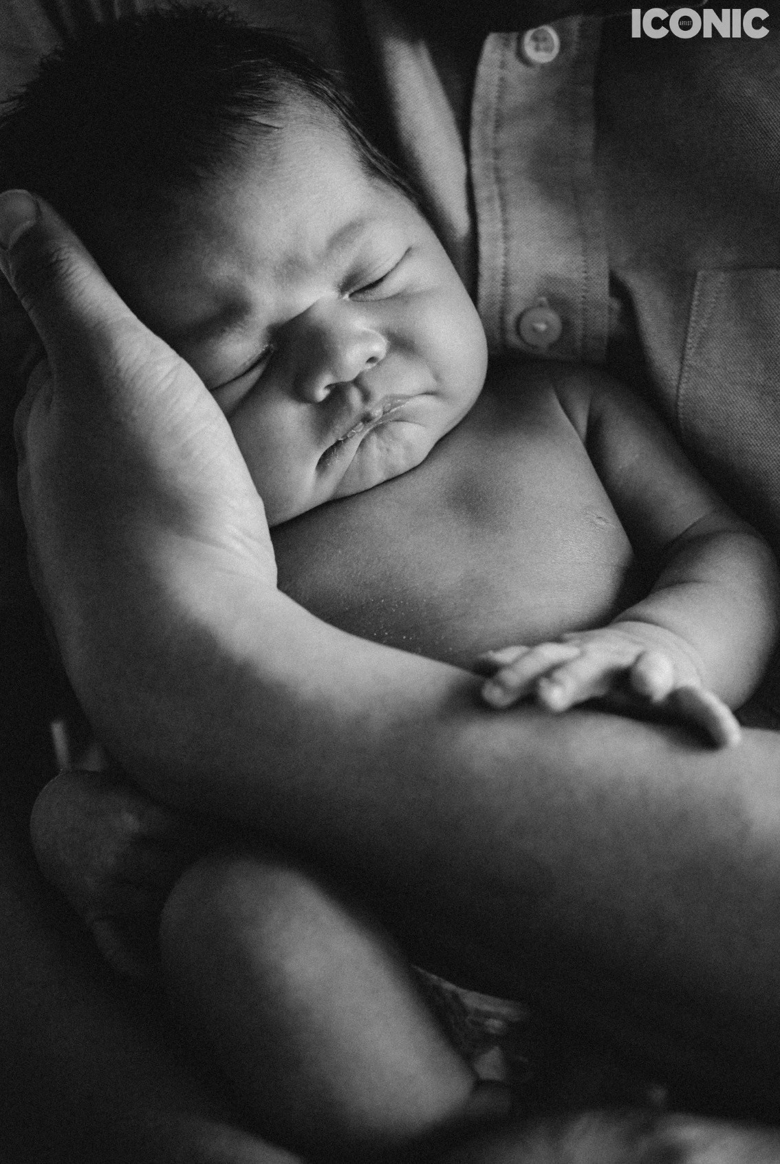 Black and white portrait of a peacefully sleeping newborn baby cradled in loving hands, newborn photography. Iconic