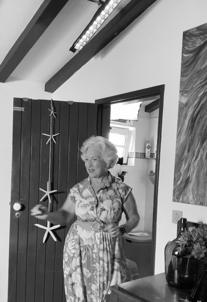 Fotografia de retrato e lifestyle a preto e branco de uma mulher sénior à porta de uma casa tradicional, produzida pela Khave Media